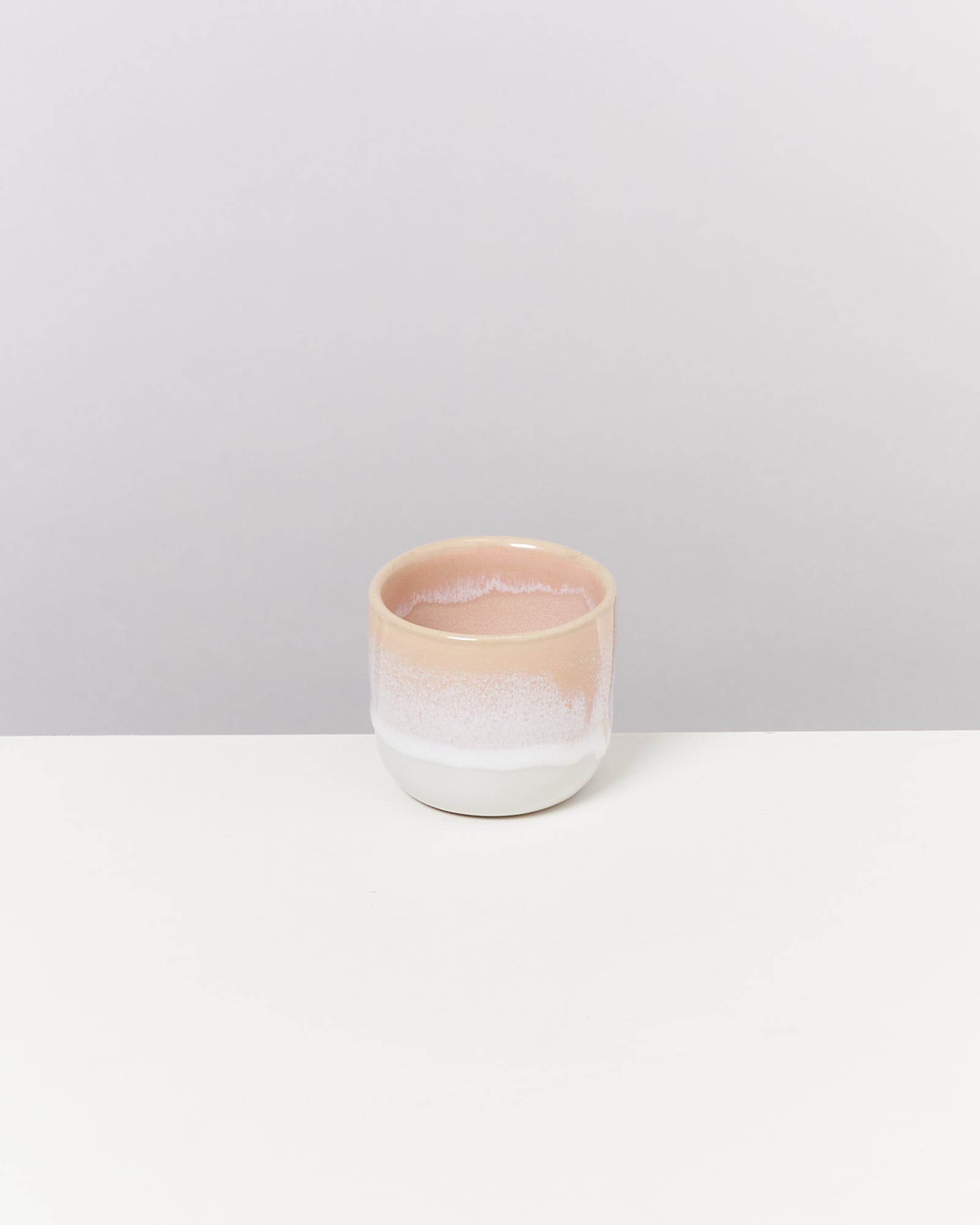 Kleine, zweifarbige Keramikschale in Rosa und Weiß auf einem weißen Tisch vor grauem Hintergrund.