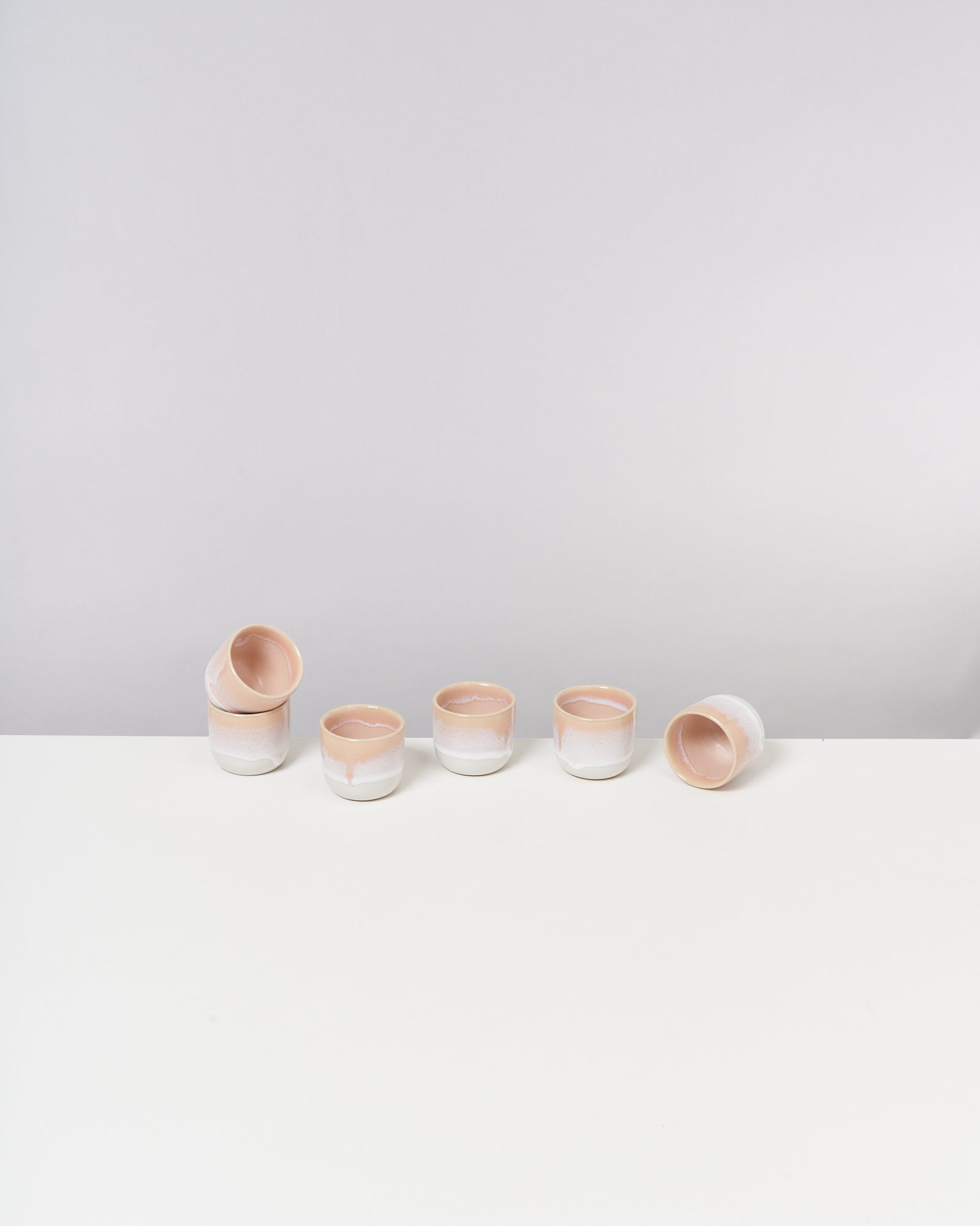 Sechs pastellfarbene Keramiktassen auf weißem Untergrund, teilweise gestapelt und liegend.