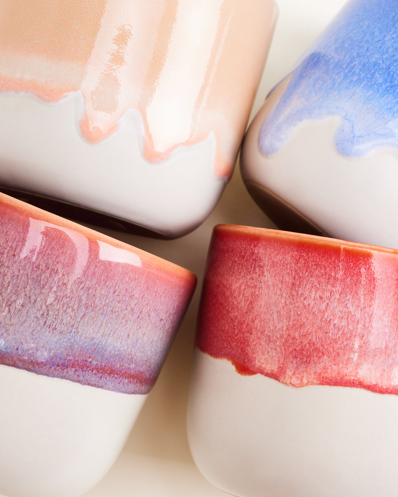 Vier Keramikgefäße mit bunten Glasuren in Blau, Rosa und Beige lehnen nebeneinander.