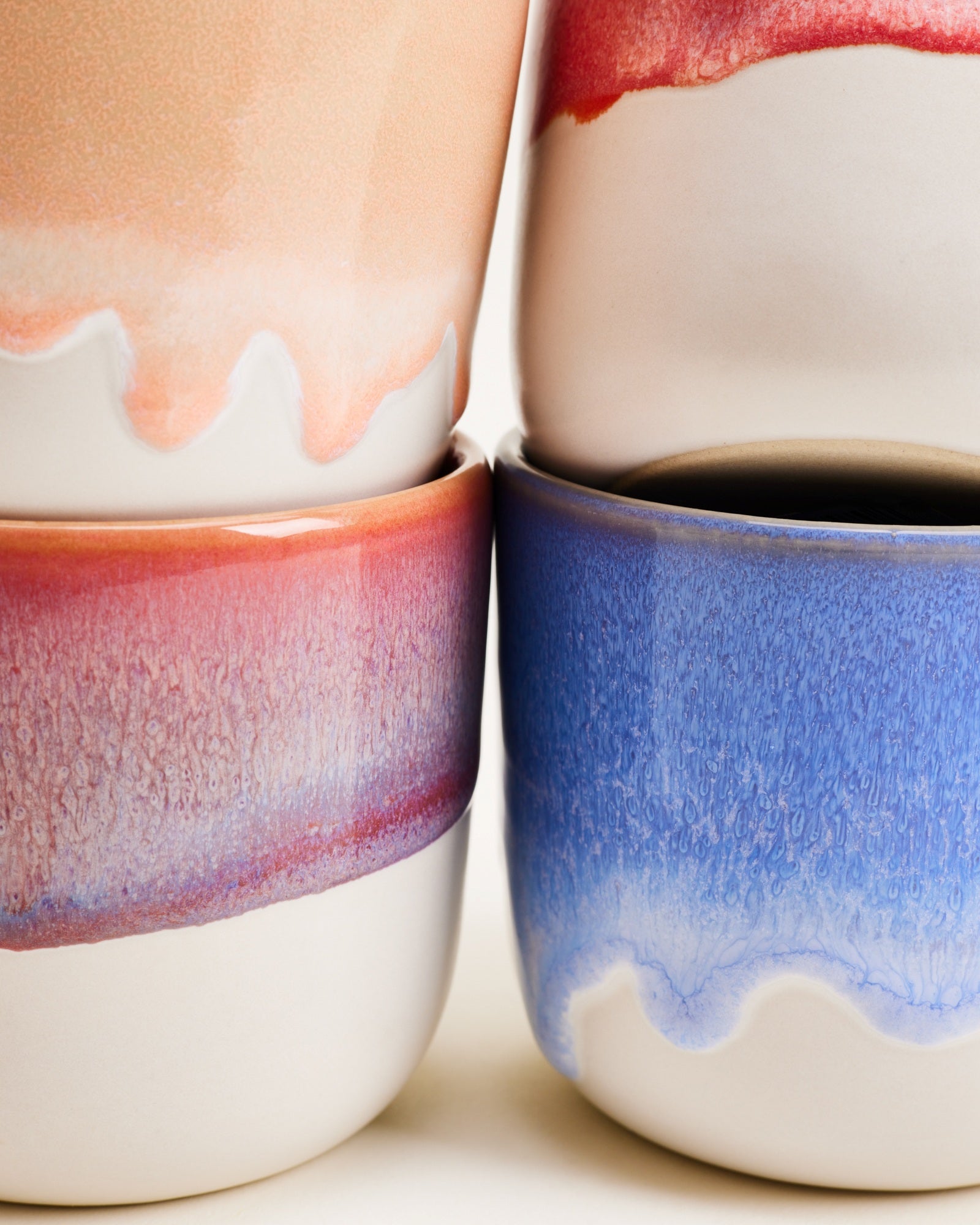 Vier Keramiktassen in Pastelltönen mit bunten, verwaschenen Glasuren stehen dicht nebeneinander.