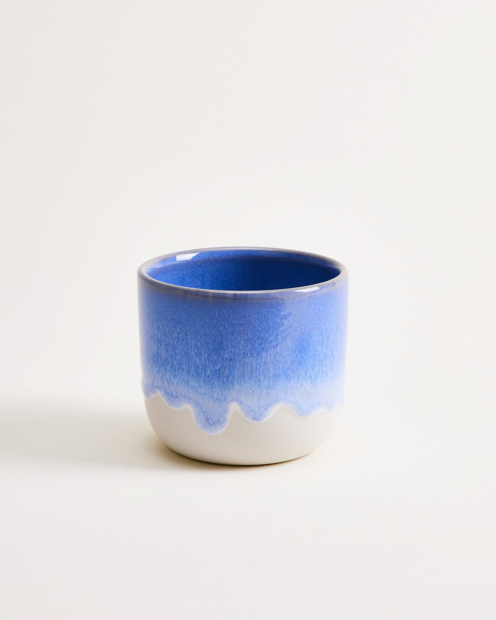 Blauer und weißer Keramikbecher mit gewelltem Design auf hellem Hintergrund.