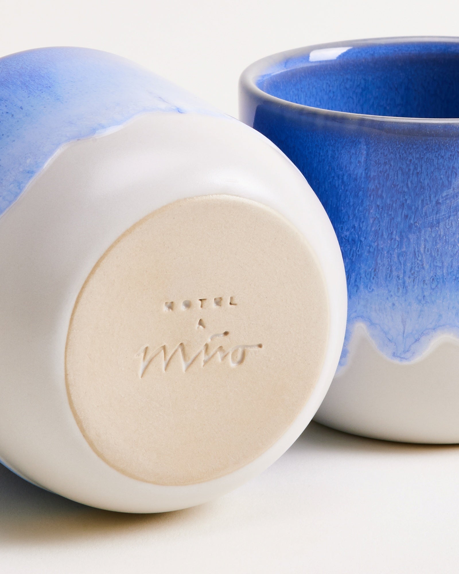 Zwei blau-weiße Keramiktassen, eine liegt auf der Seite mit der Prägung "Hotel A Miro" sichtbar.