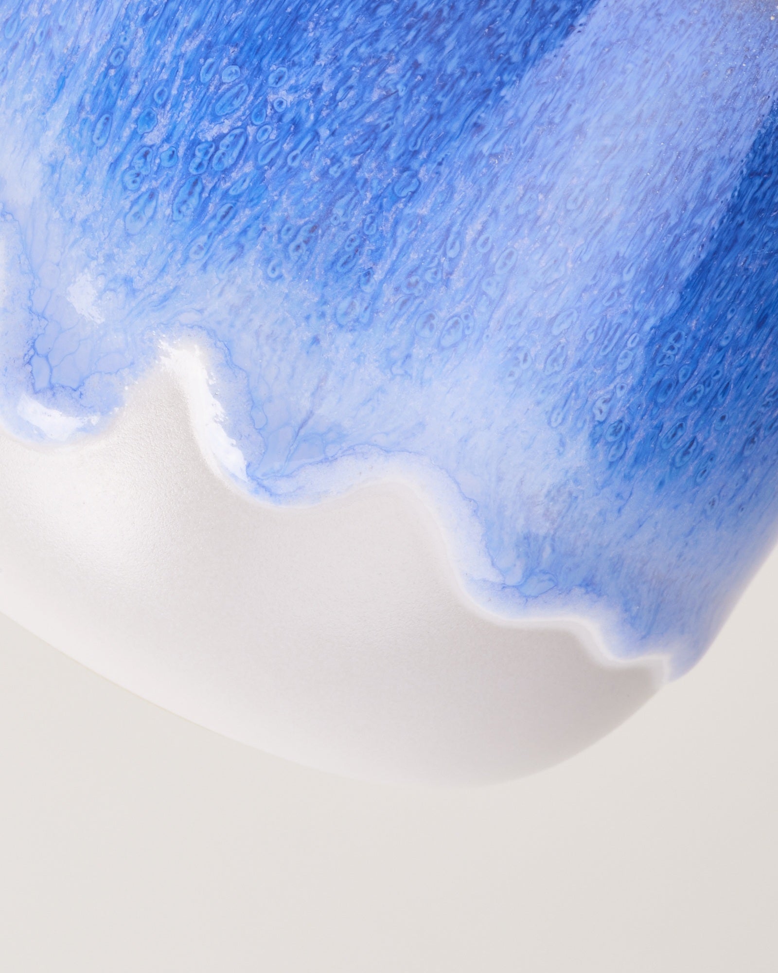 Nahaufnahme einer blauen Keramikvase mit weißen, wellenförmigen Details.