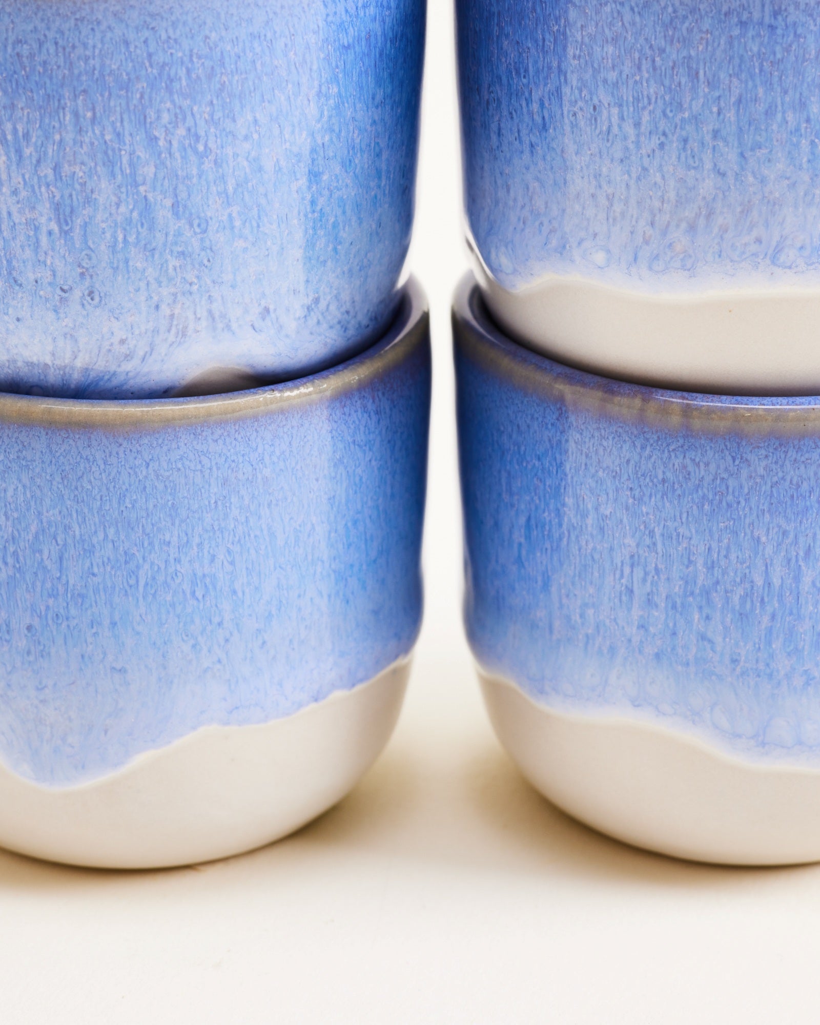 Vier stapelbare, blau-weiße Keramiktassen mit glasiertem Finish, in Nahaufnahme dargestellt.