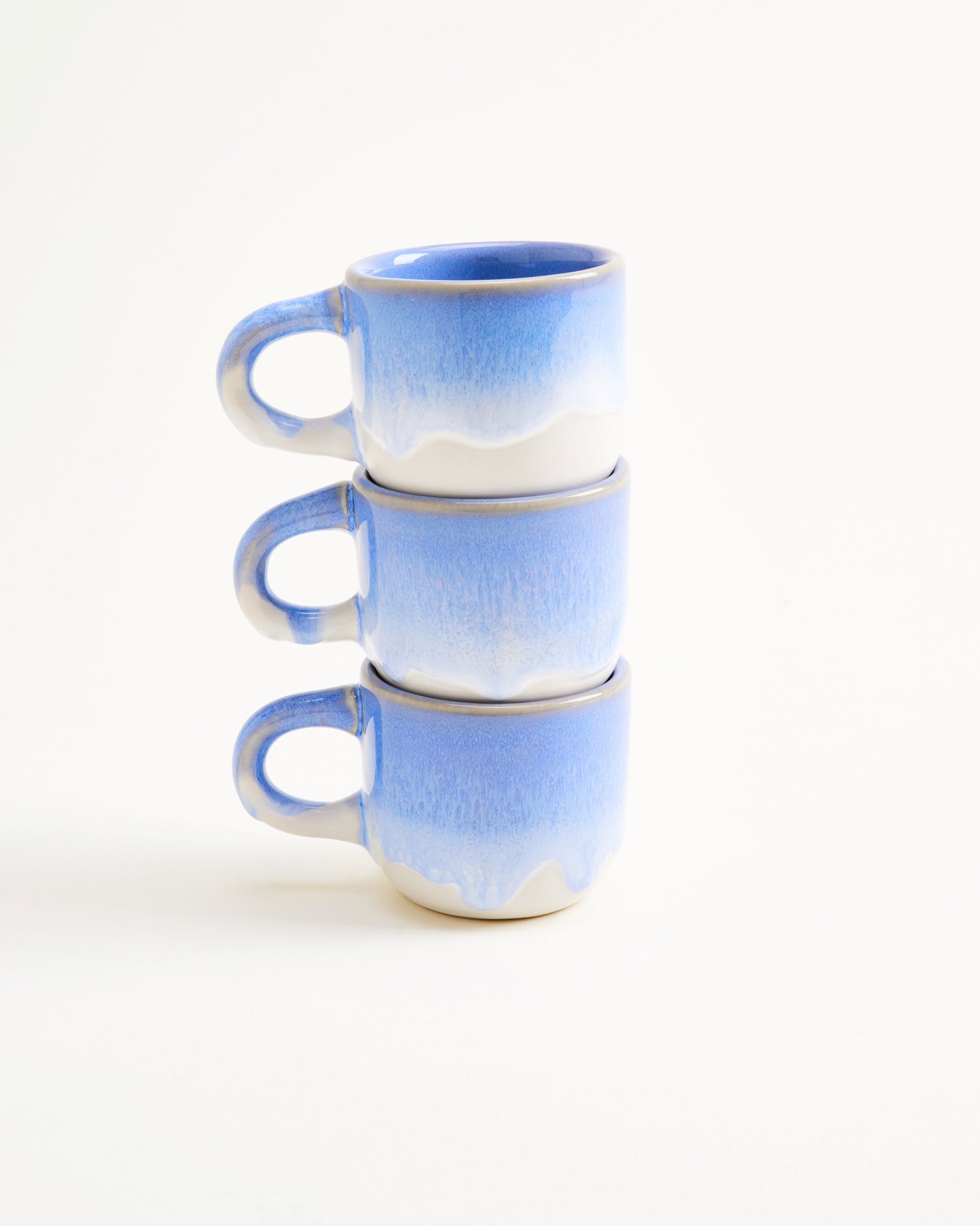 Drei gestapelte blaue Tassen mit weißem Verlauf auf einem weißen Hintergrund.