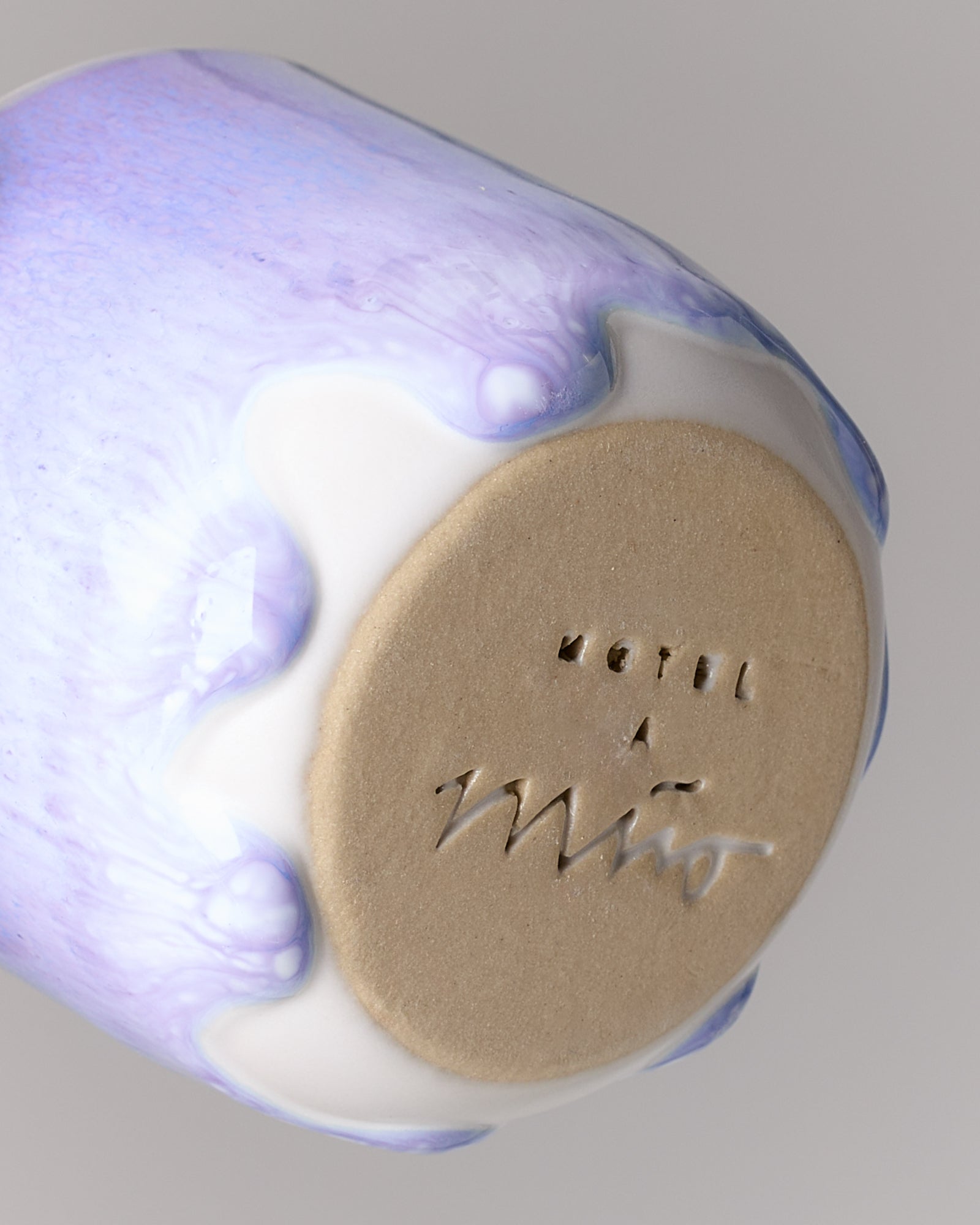 Unterseite einer Keramiktasse mit lavendelfarbenem und weißem Glanz, mit eingeprägtem Namen.