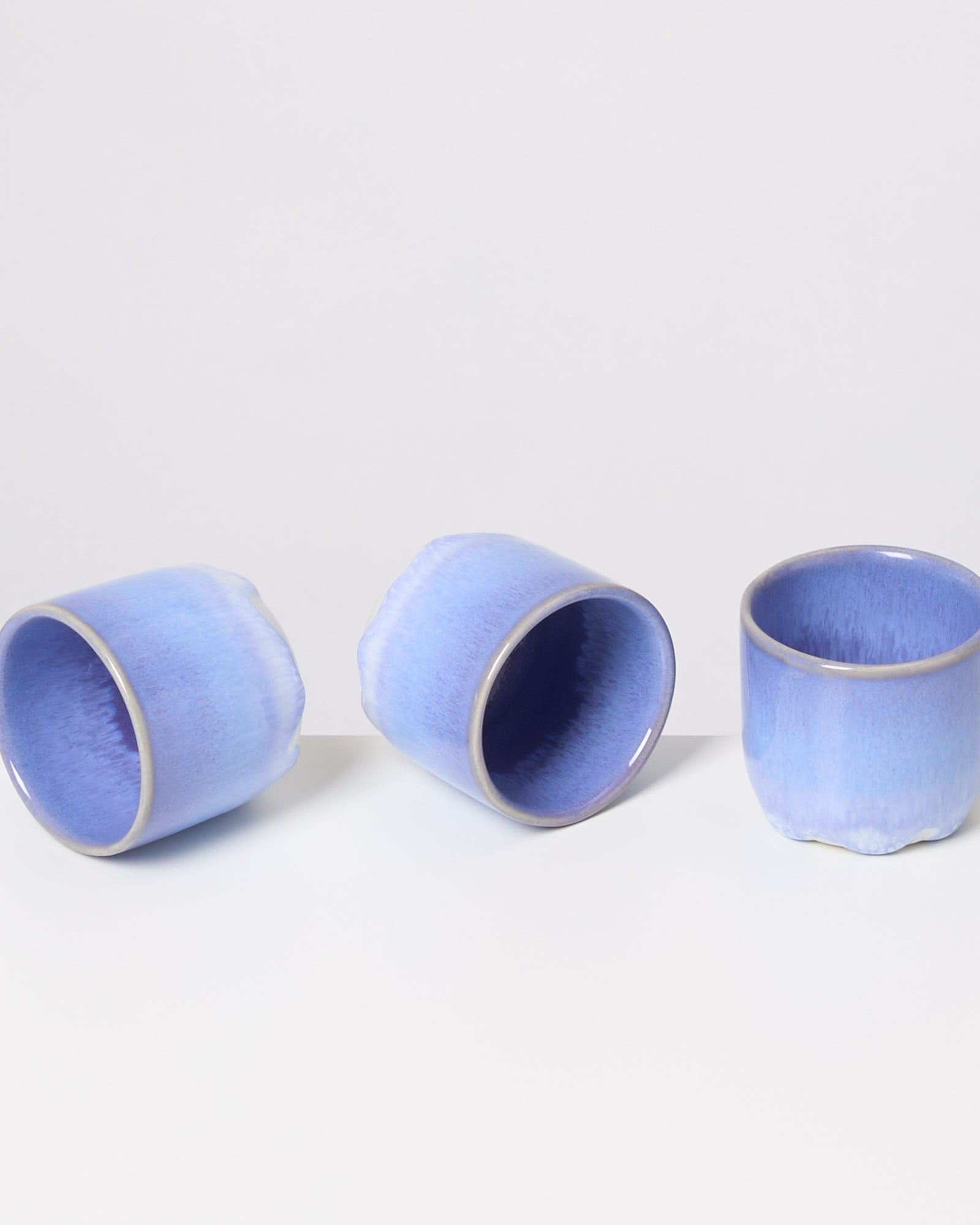 Drei blaue Keramiktassen stehen auf weißem Hintergrund, zwei liegen auf der Seite, eine steht aufrecht.