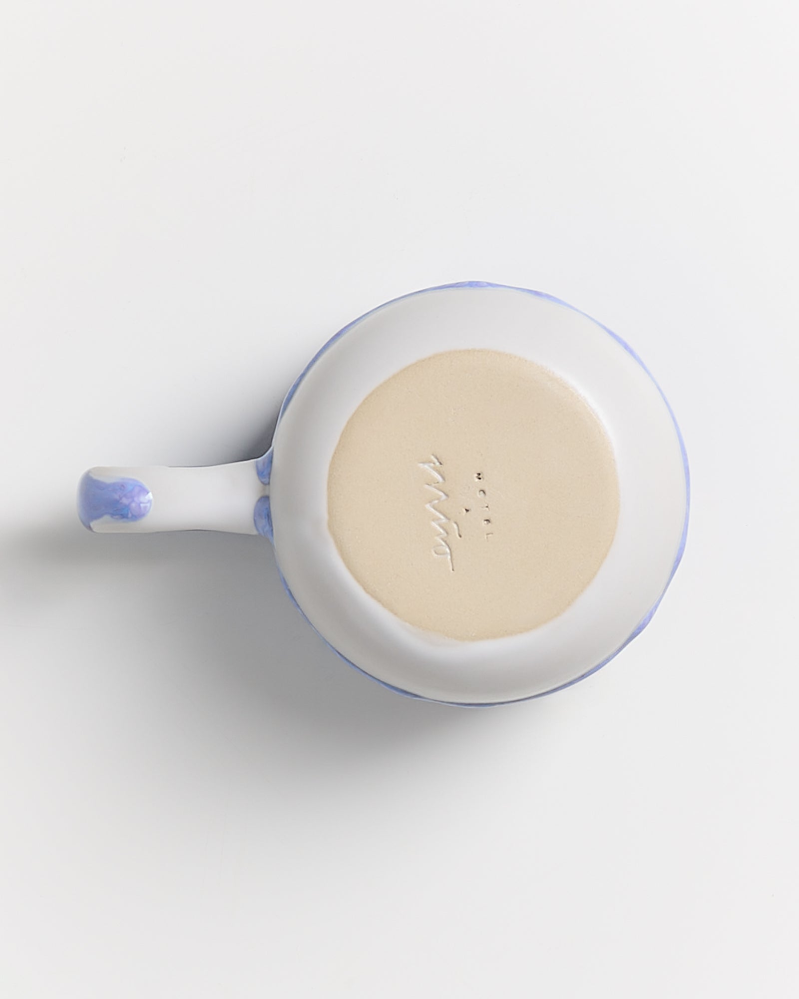 Weiße keramische Tasse mit blauem Griff, von oben fotografiert, zeigt die Unterseite mit eingraviertem Text.