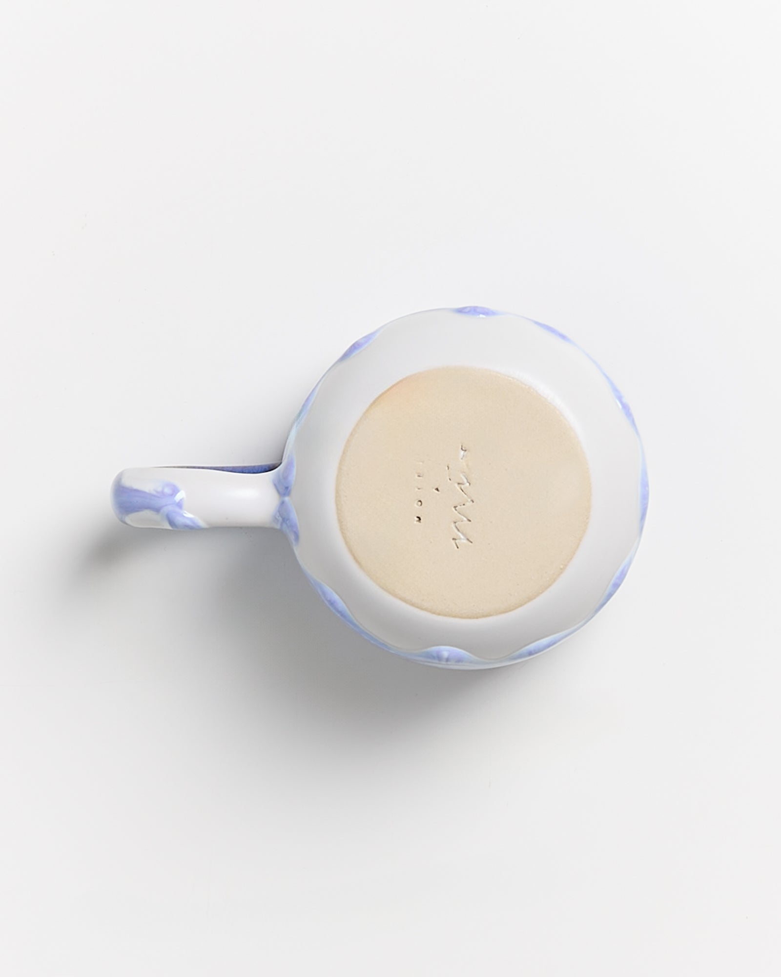 Unterseite einer Tasse mit blau-weißem Muster und Henkel, auf hellem Hintergrund.