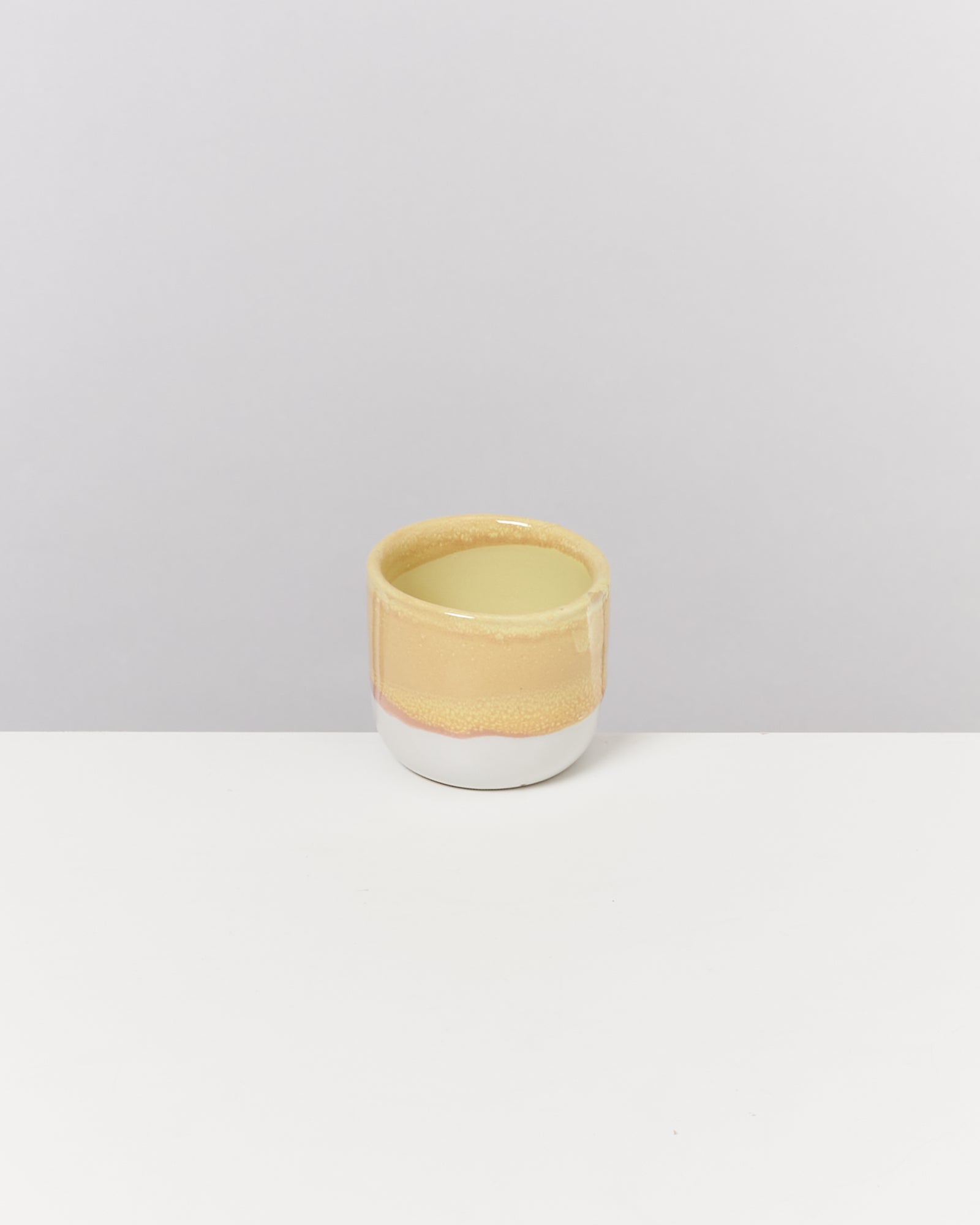 Keramiktasse in Beige und Weiß auf weißem Hintergrund.