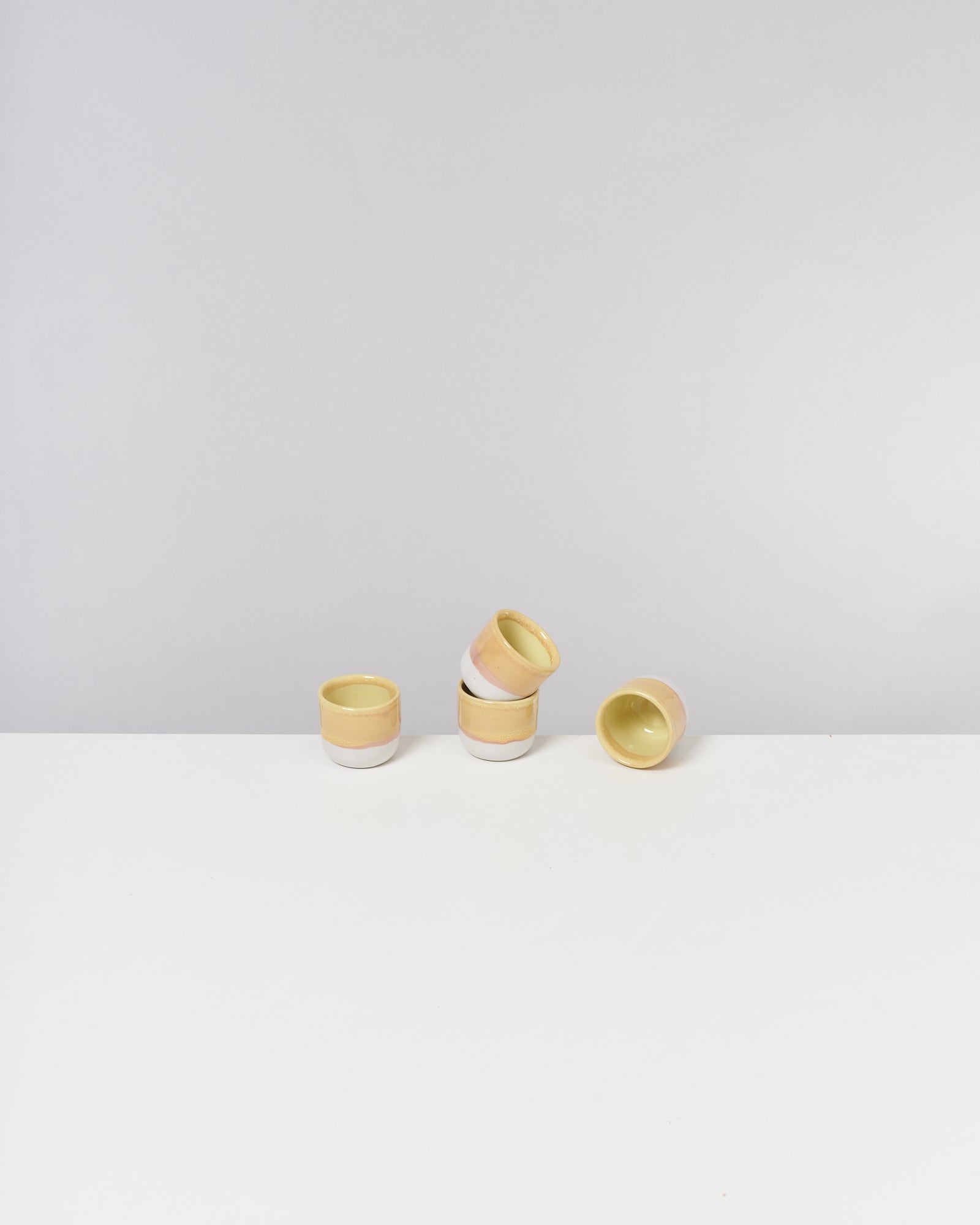Vier kleine Tassen, die unterschiedlich ausgerichtet auf einem weißen Tisch stehen.