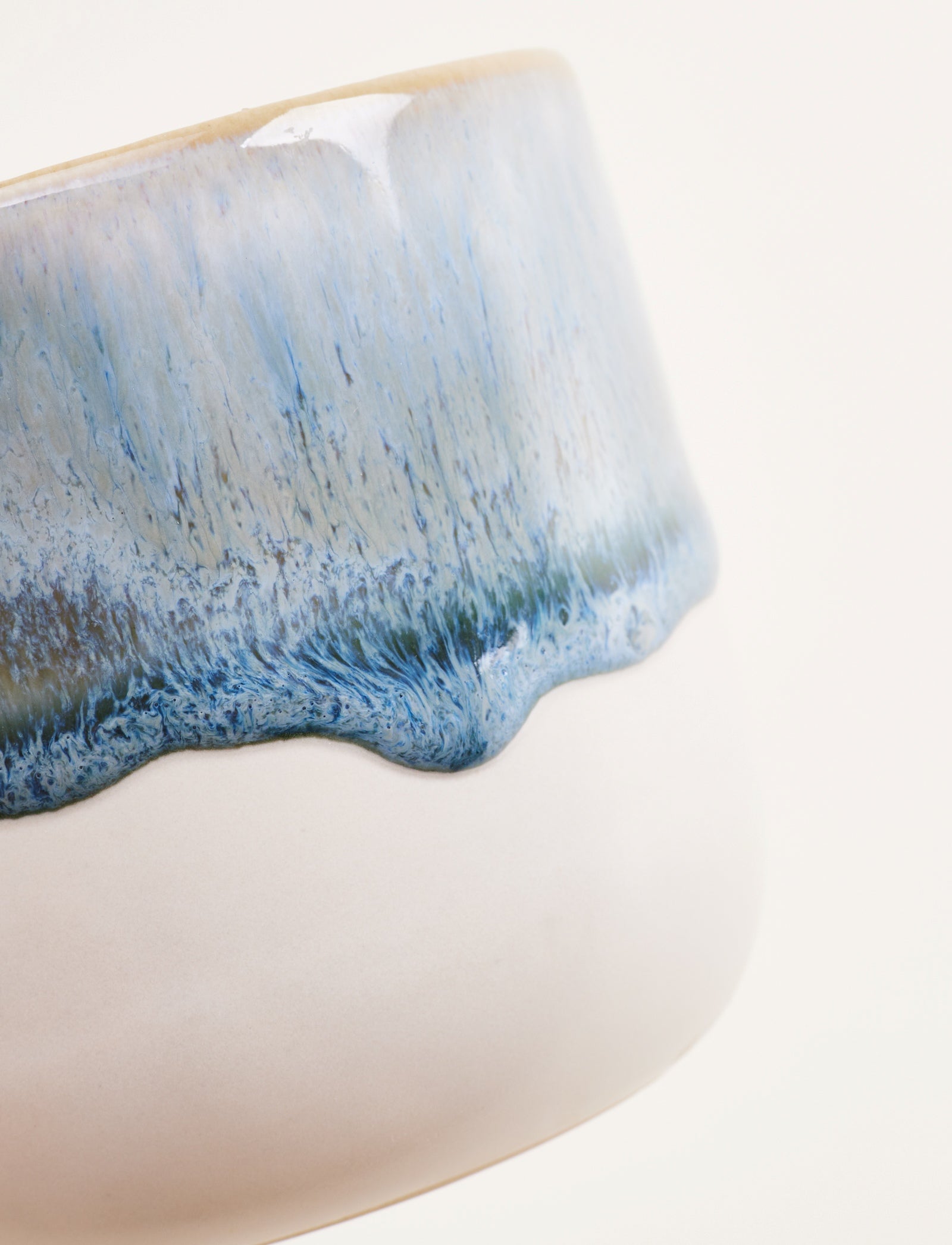 Nahaufnahme einer Keramiktasse mit blauem, glasiertem Randmuster auf weißem Hintergrund.