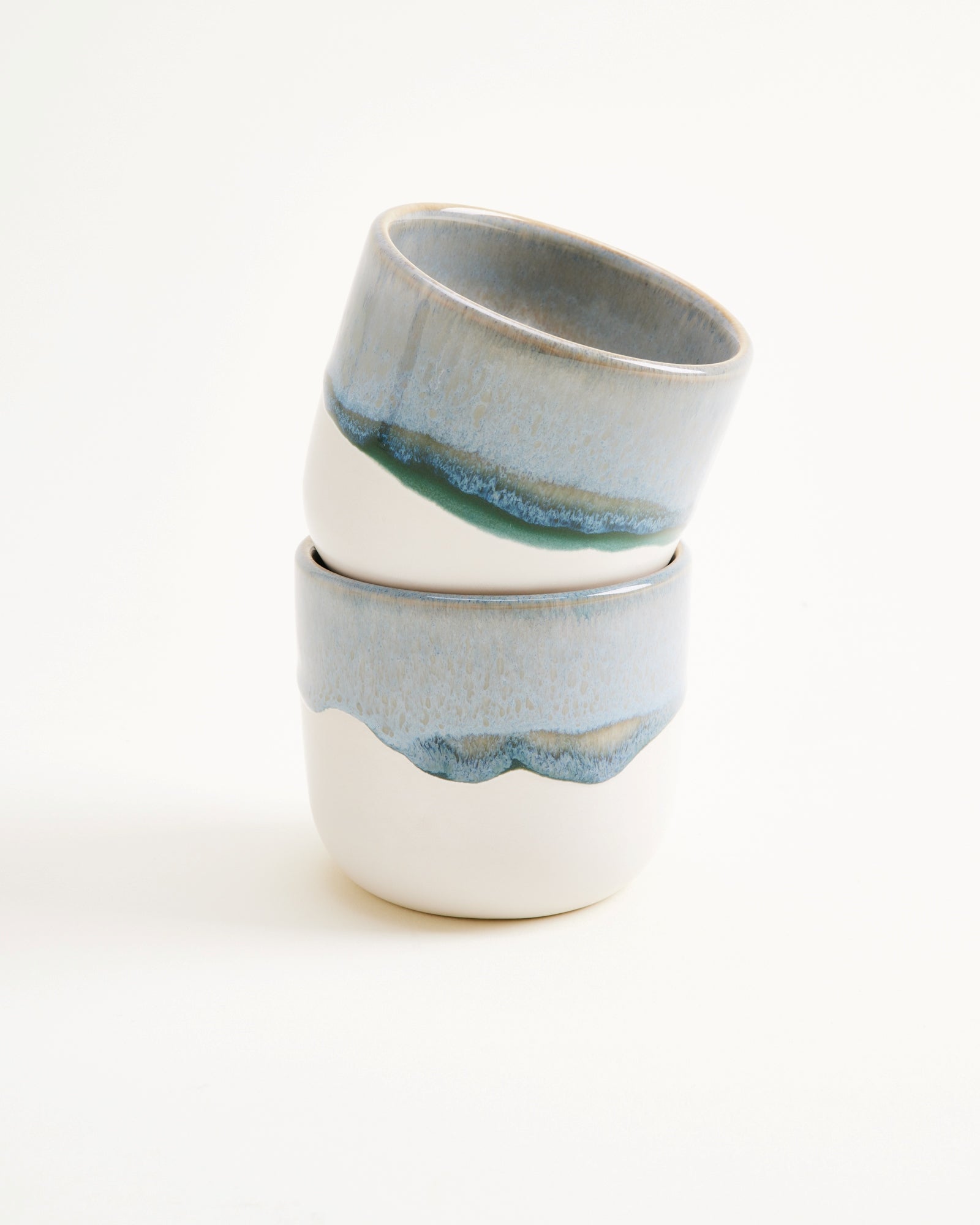 Zwei gestapelte, blau-weiße Keramikbecher mit wellenförmigem Muster auf hellem Hintergrund.