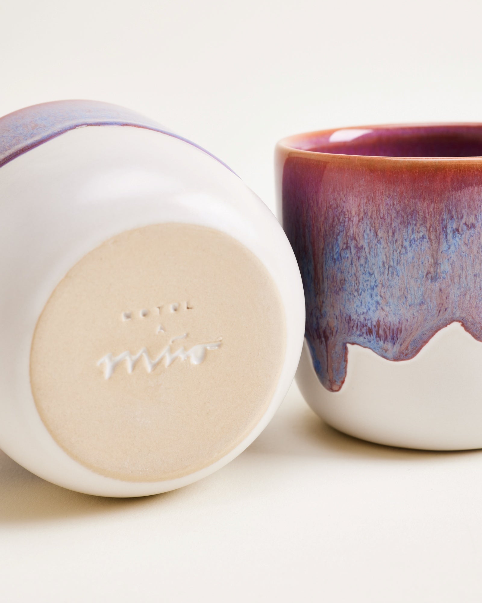 Zwei bunte Keramikbecher, einer auf der Seite liegend mit der Aufschrift "mio" am Boden.
