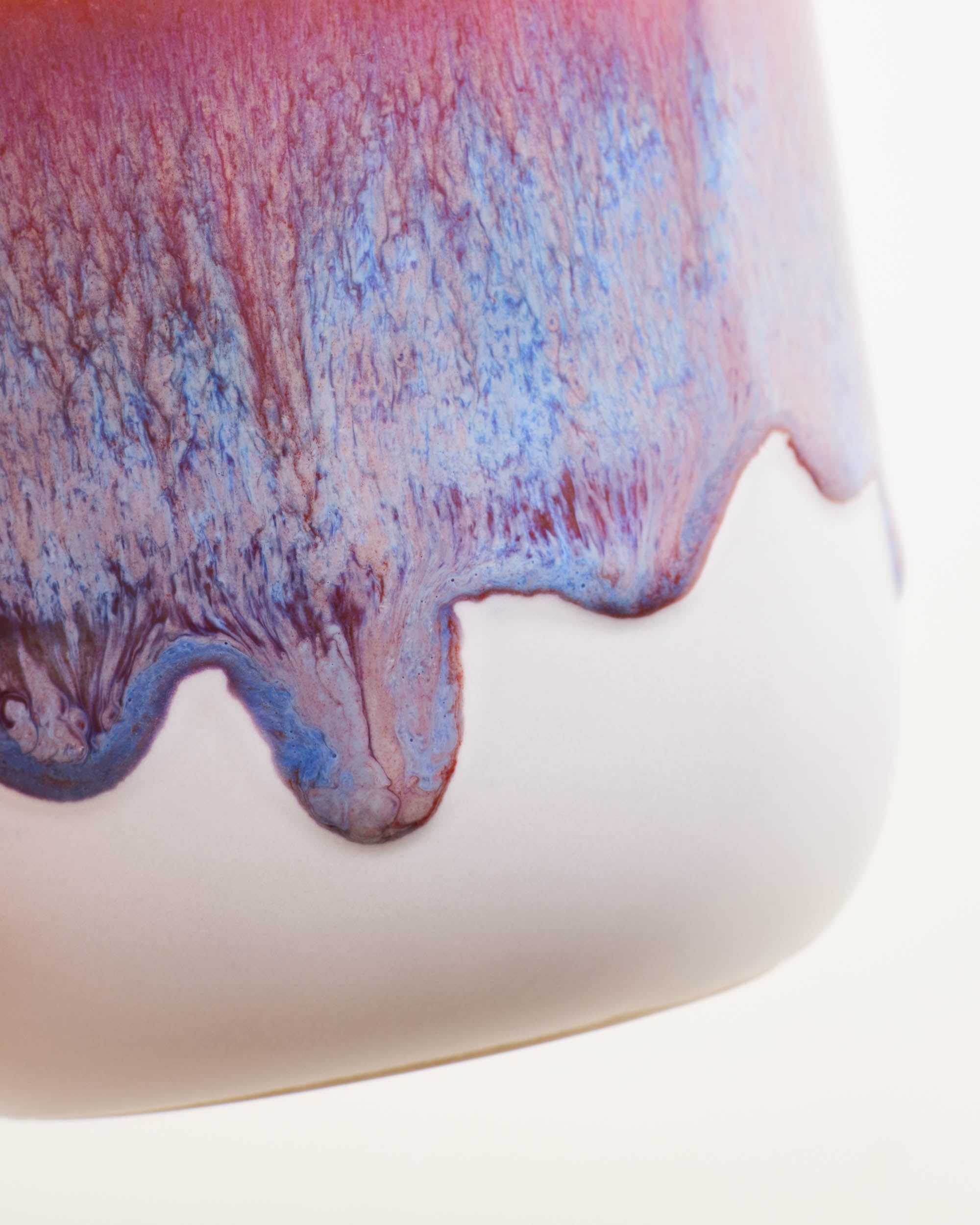 Nahaufnahme einer Keramikvase mit verlaufender Glasur in Rot- und Blautönen auf weißem Untergrund.