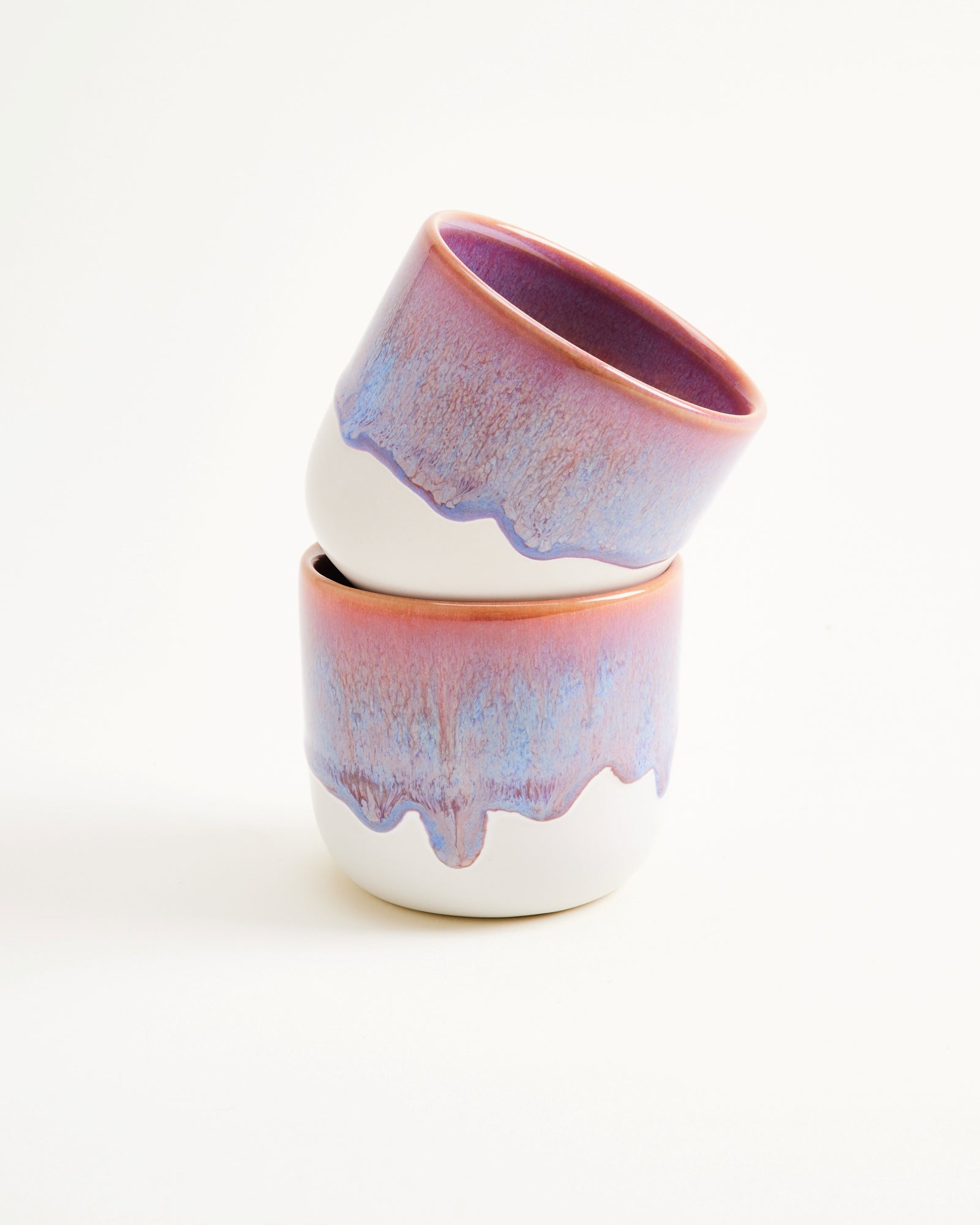 Zwei gestapelte Keramiktassen mit rosa-blauer Glasur auf weißem Hintergrund.