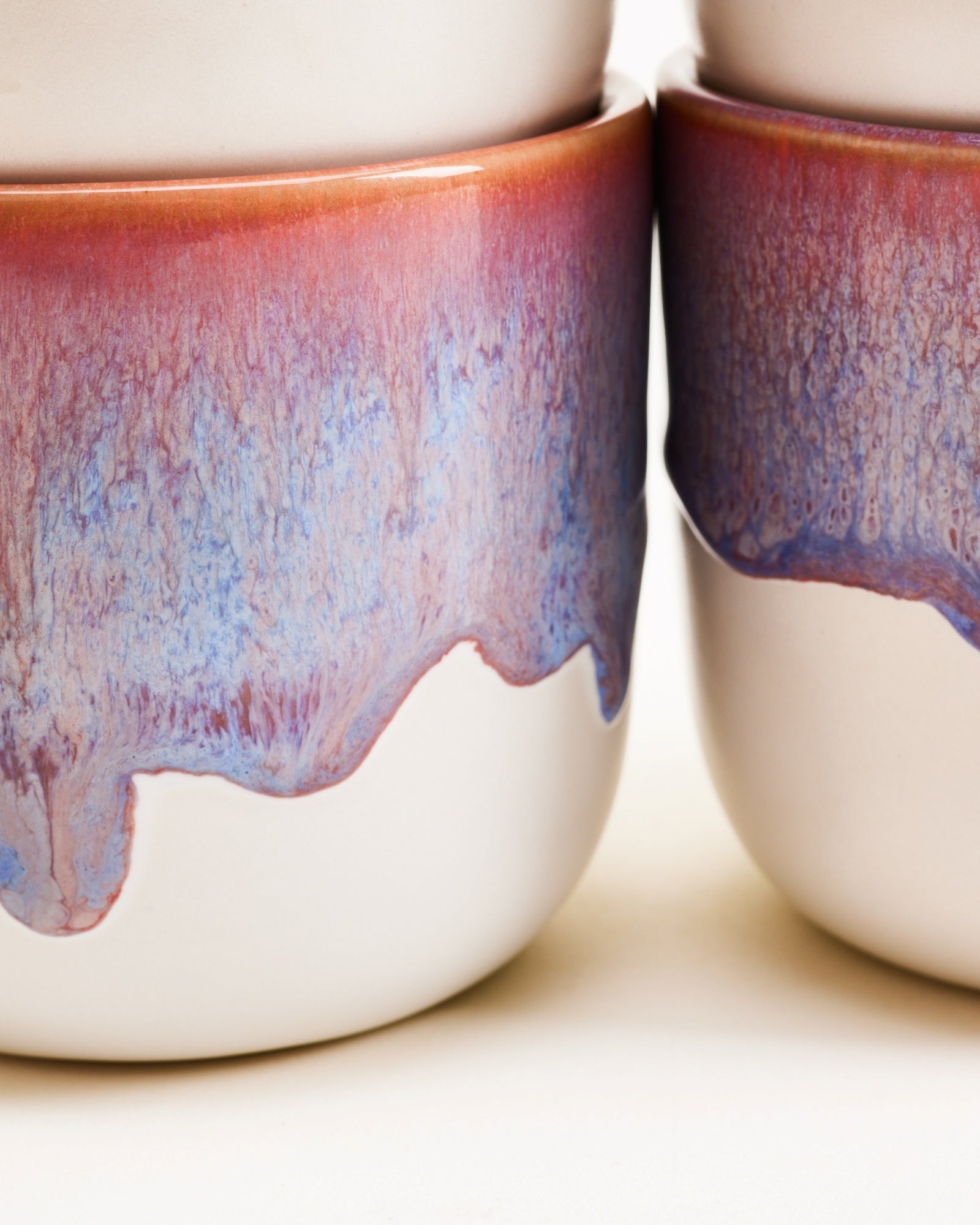 Nahaufnahme von Keramikbechern mit fließender Glasur in Blau- und Rottönen.