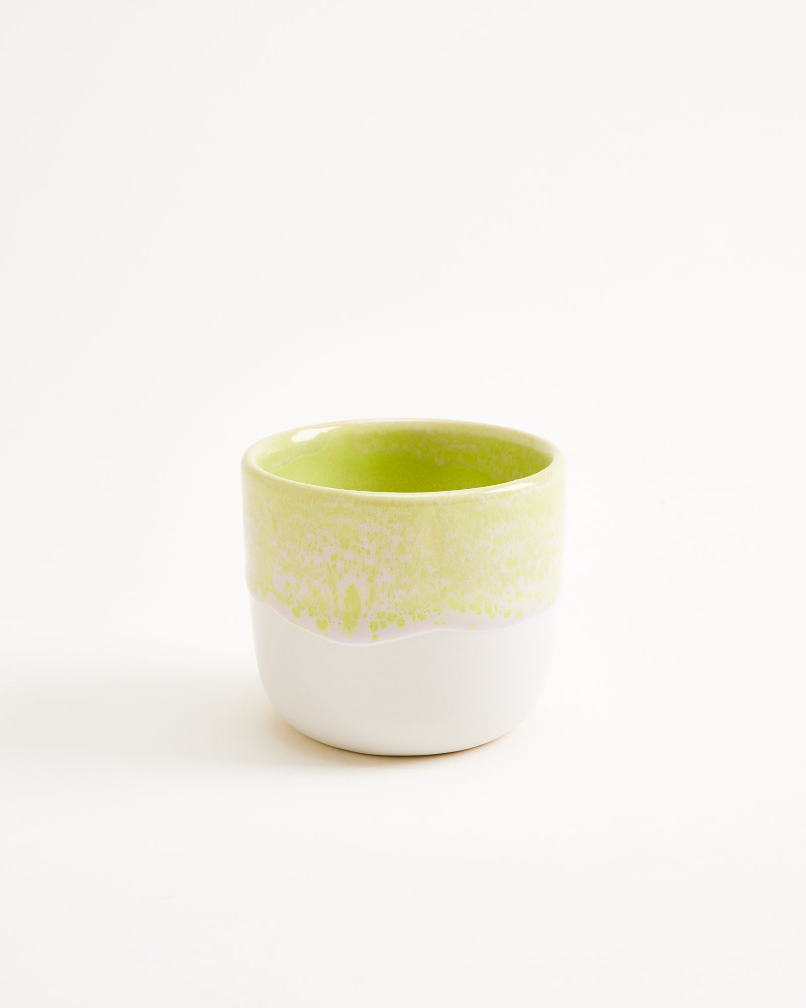 Kleine Keramiktasse mit grünlichem Oberteil und weißem Unterteil auf weißem Hintergrund.