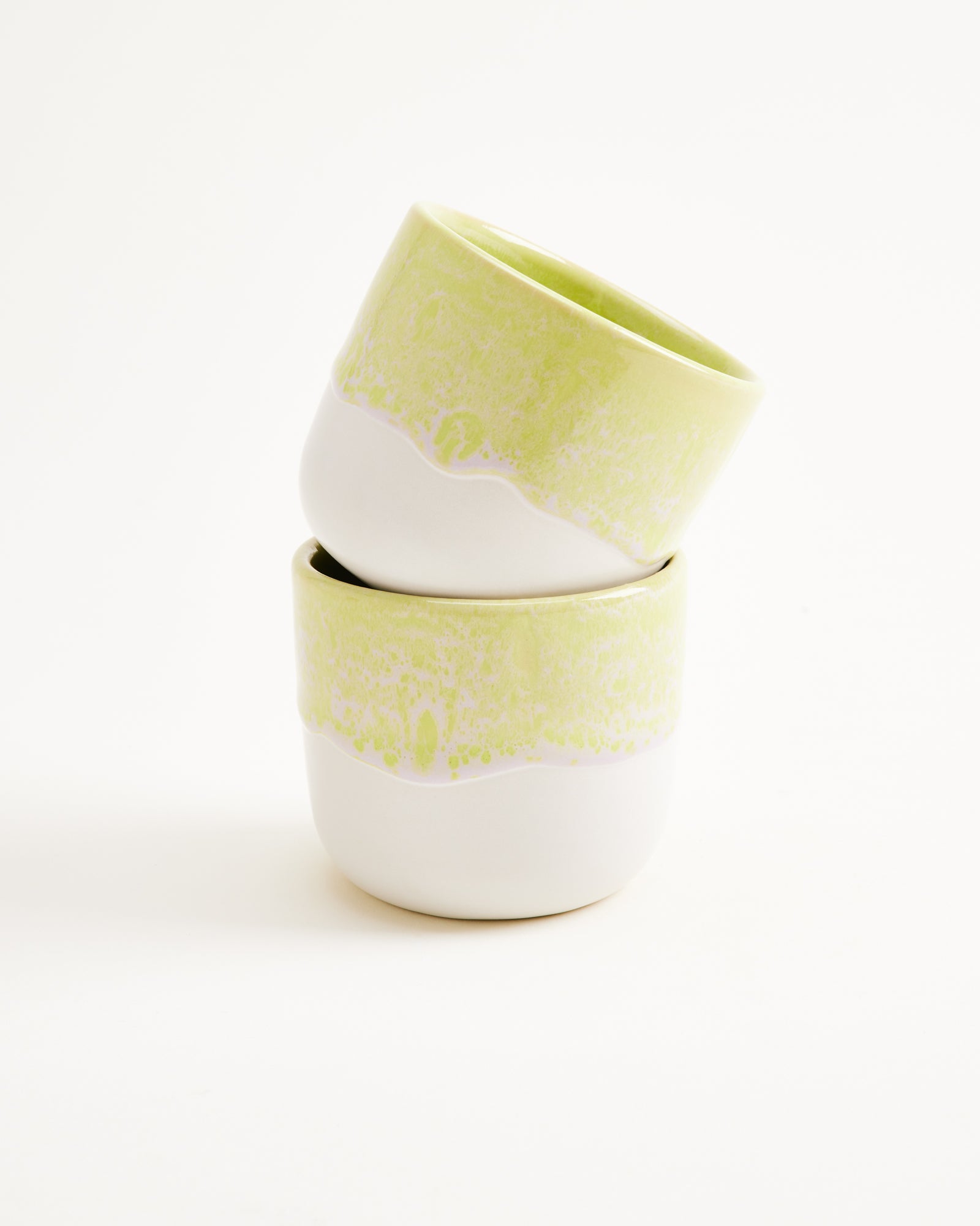 Zwei gestapelte, pastellgrüne Keramikbecher vor einem weißen Hintergrund.