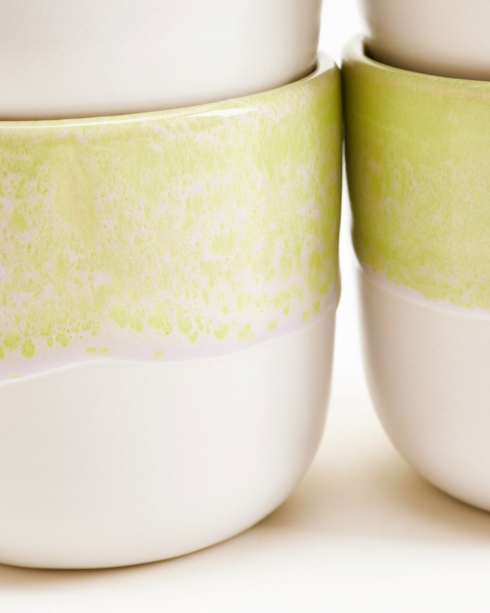 Nahaufnahme von gestapelten weißen Keramiktassen mit grünlich-gelber Glasur.
