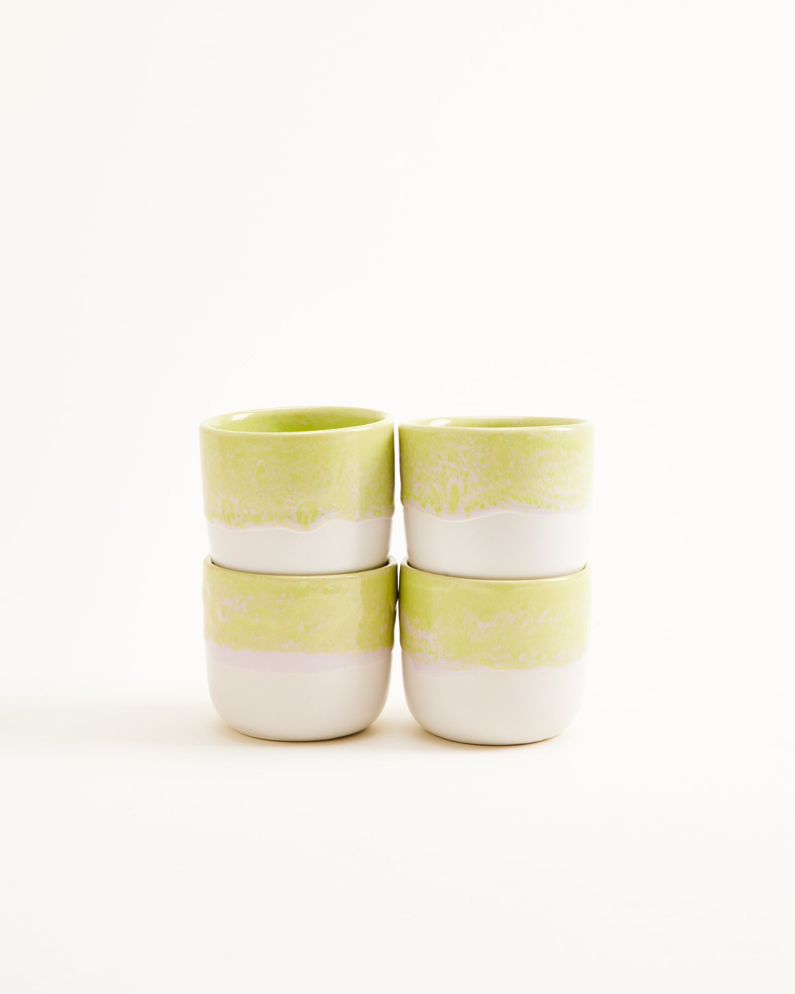 Vier gestapelte Keramiktassen mit grün-weißer Glasur vor weißem Hintergrund.