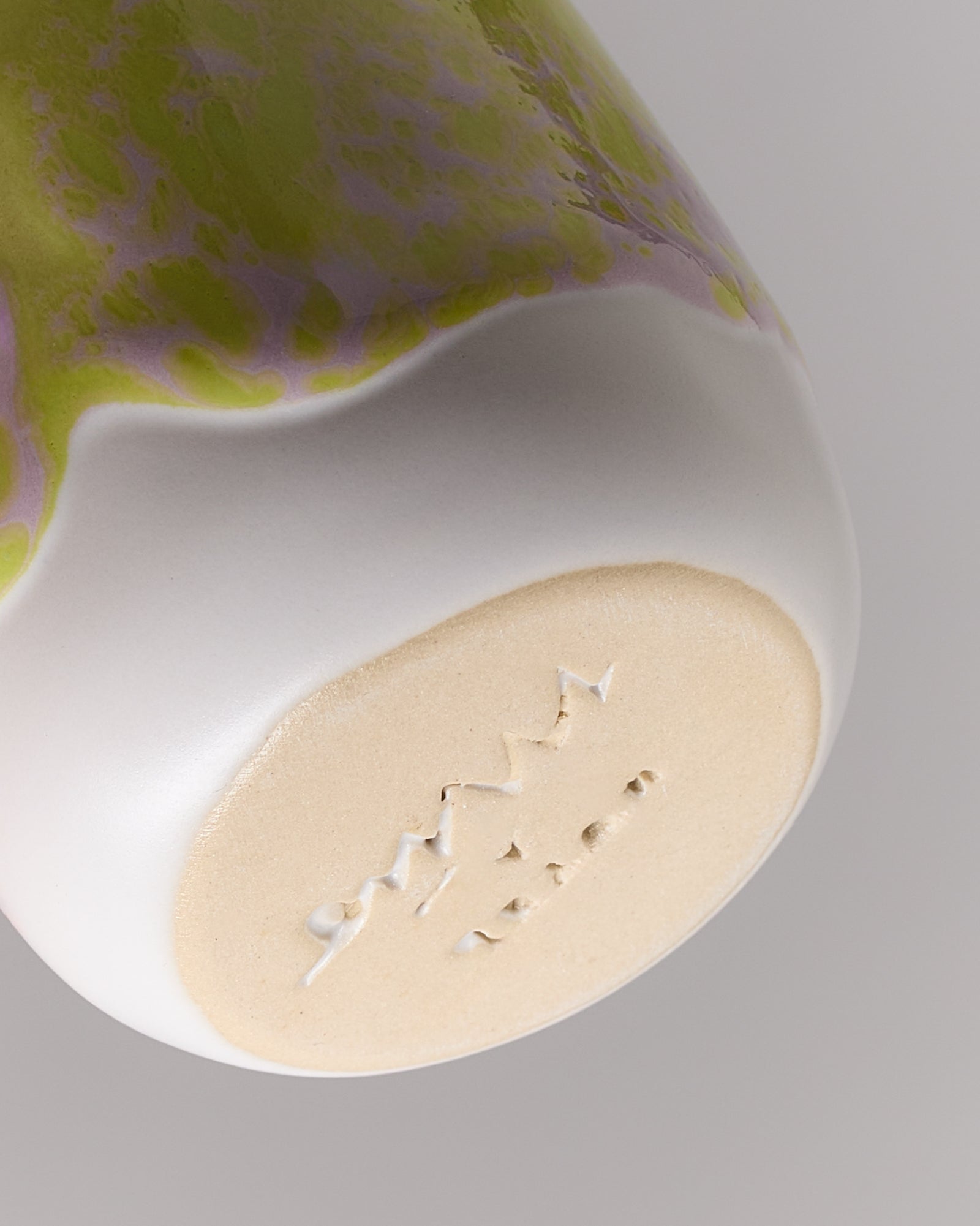 Nahaufnahme eines bemalten Keramikbechers mit grünen und lila Mustern und einem rohen, unglasierten Boden.