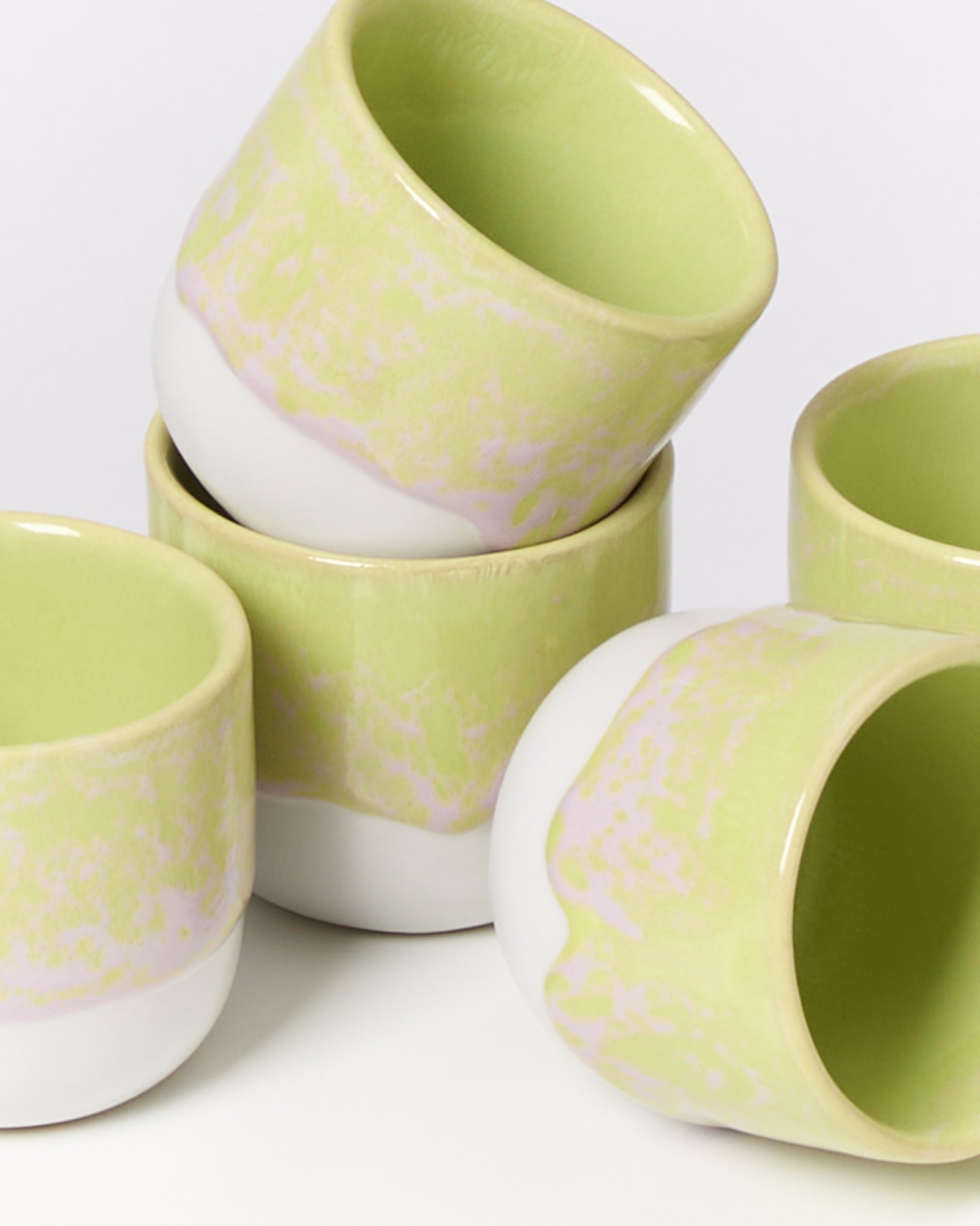 Fünf pastellgrüne und weiße Keramiktassen, die kunstvoll gestapelt sind.
