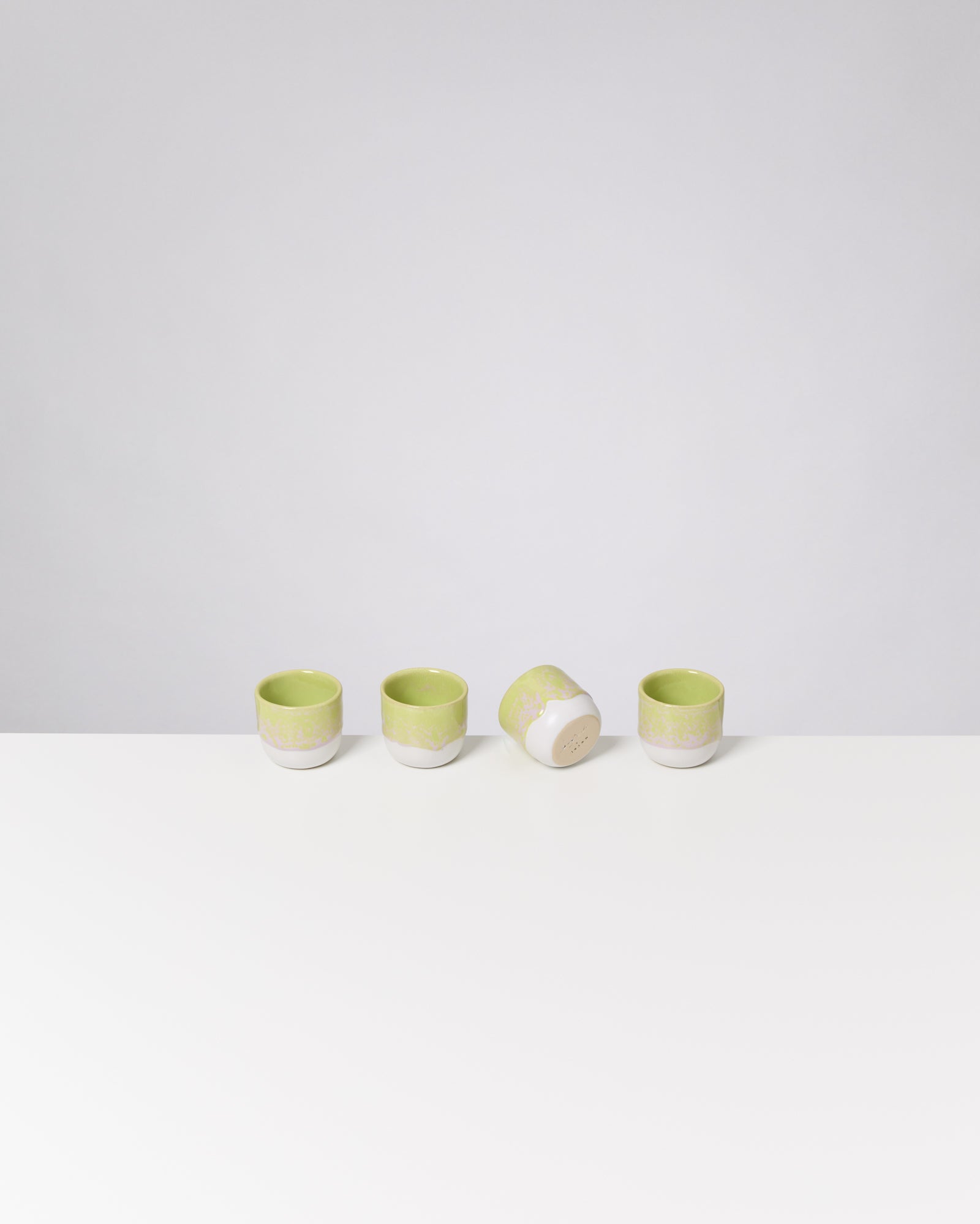 Vier grüne Teetassen auf einem weißen Tisch, eine davon liegt seitlich.