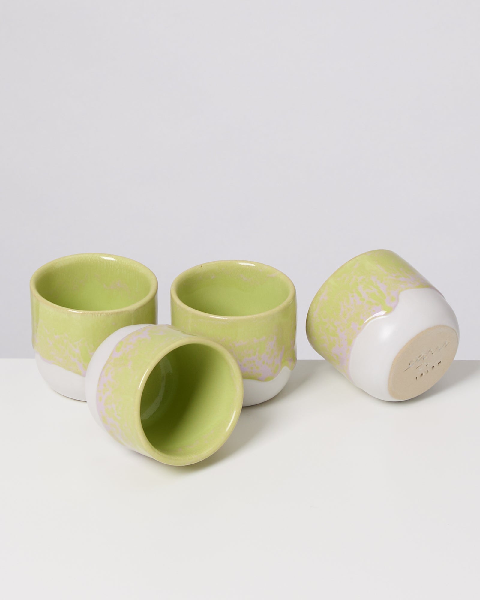 Vier grün-weiße Keramikbecher auf einem weißen Untergrund, drei stehend und einer liegend.