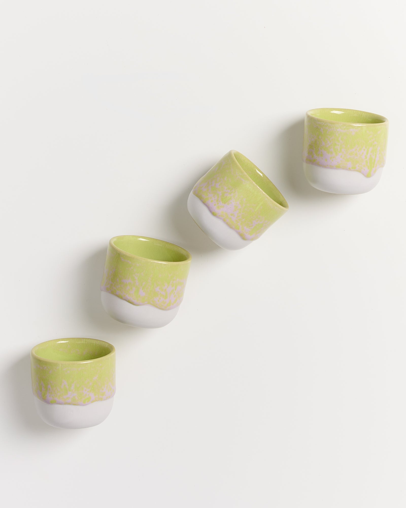Vier grün-weiße Tassen in diagonaler Anordnung auf weißem Hintergrund.