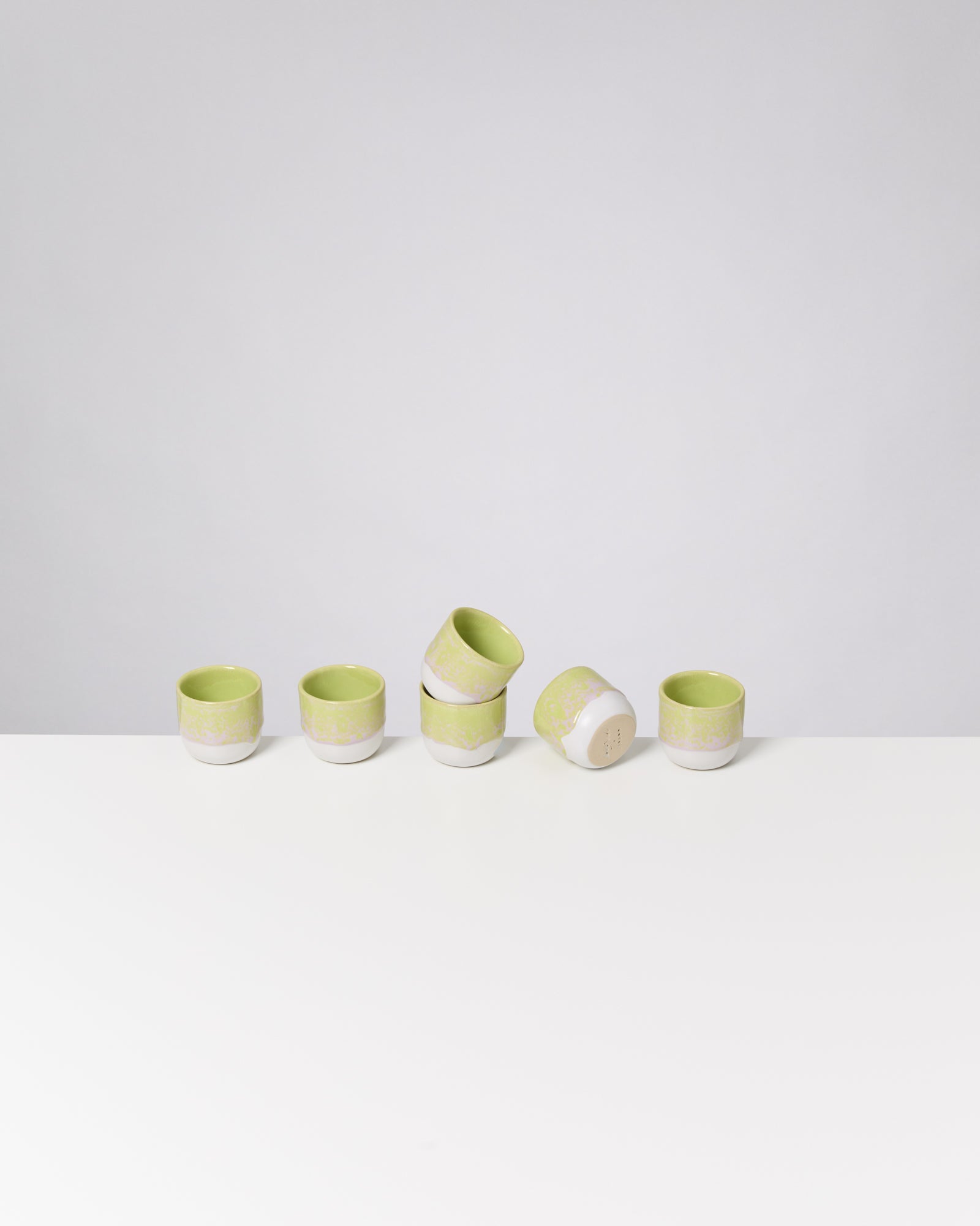 Fünf grün-weiße Keramiktassen auf einem weißen Tisch, zwei davon sind übereinander gestapelt.