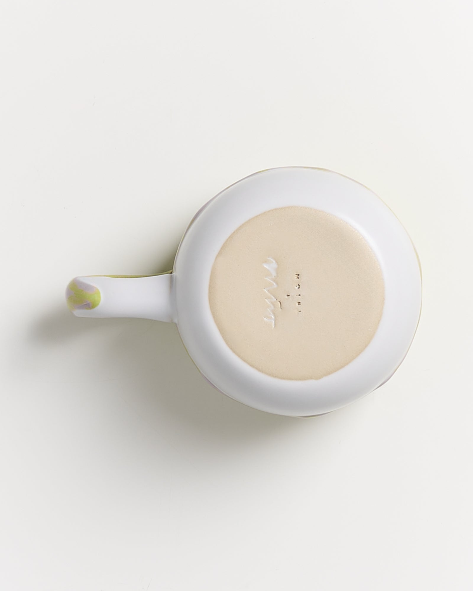 Weiße Tasse von unten fotografiert, mit beige Unterseite und geprägtem Text, auf hellem Hintergrund.