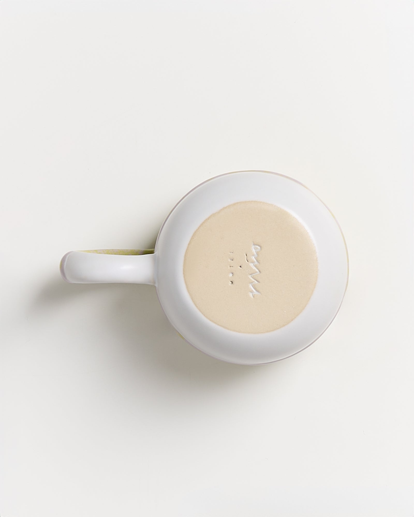 Weiße Tasse von oben gesehen auf einer hellen Oberfläche, mit sichtbarem Boden und Schriftzug.