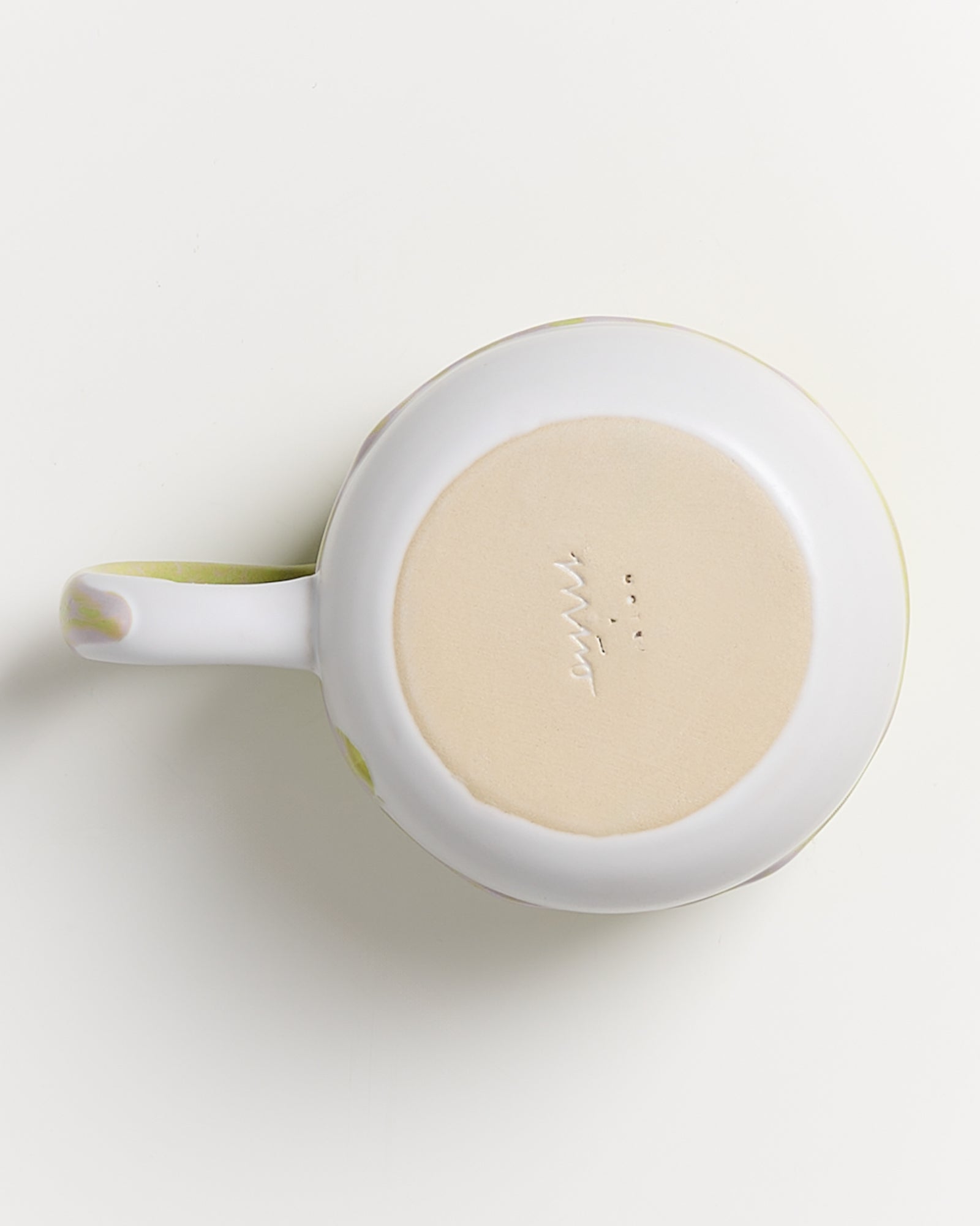 Unterseite einer weißen Tasse mit einem beigen, unlackierten Boden und einem sichtbaren Henkel auf einem weißen Hintergrund.