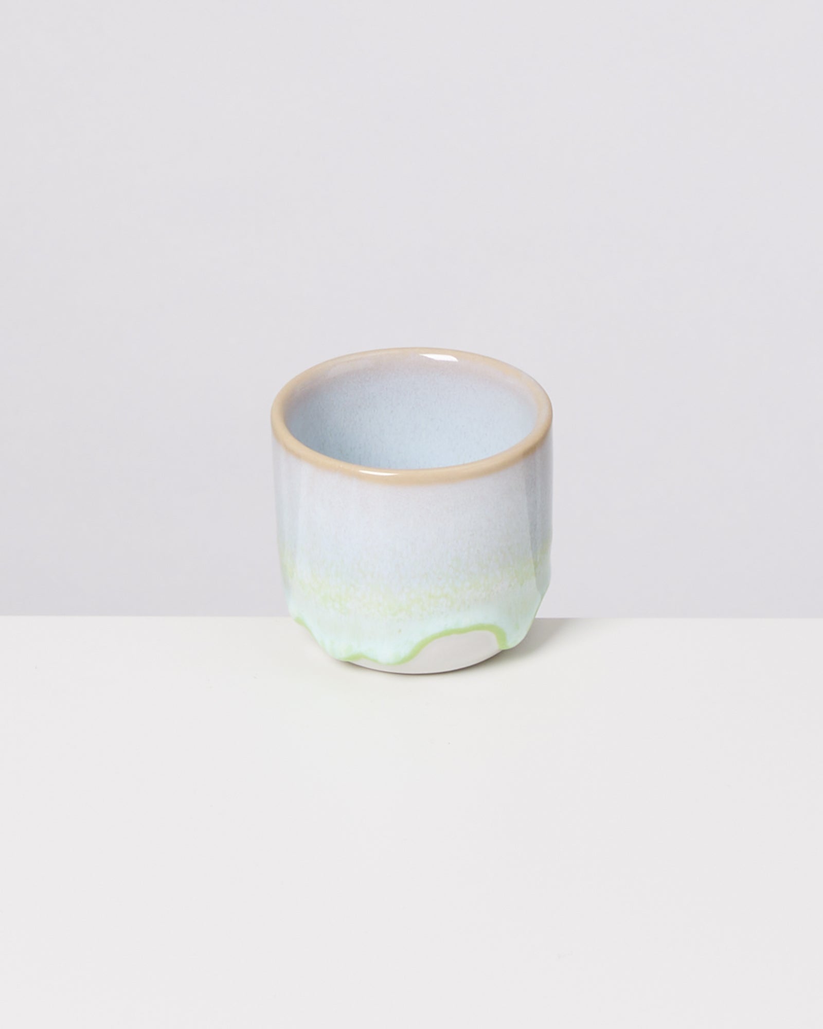 Keramiktasse mit blau-grünem Farbverlauf auf weißem Hintergrund.