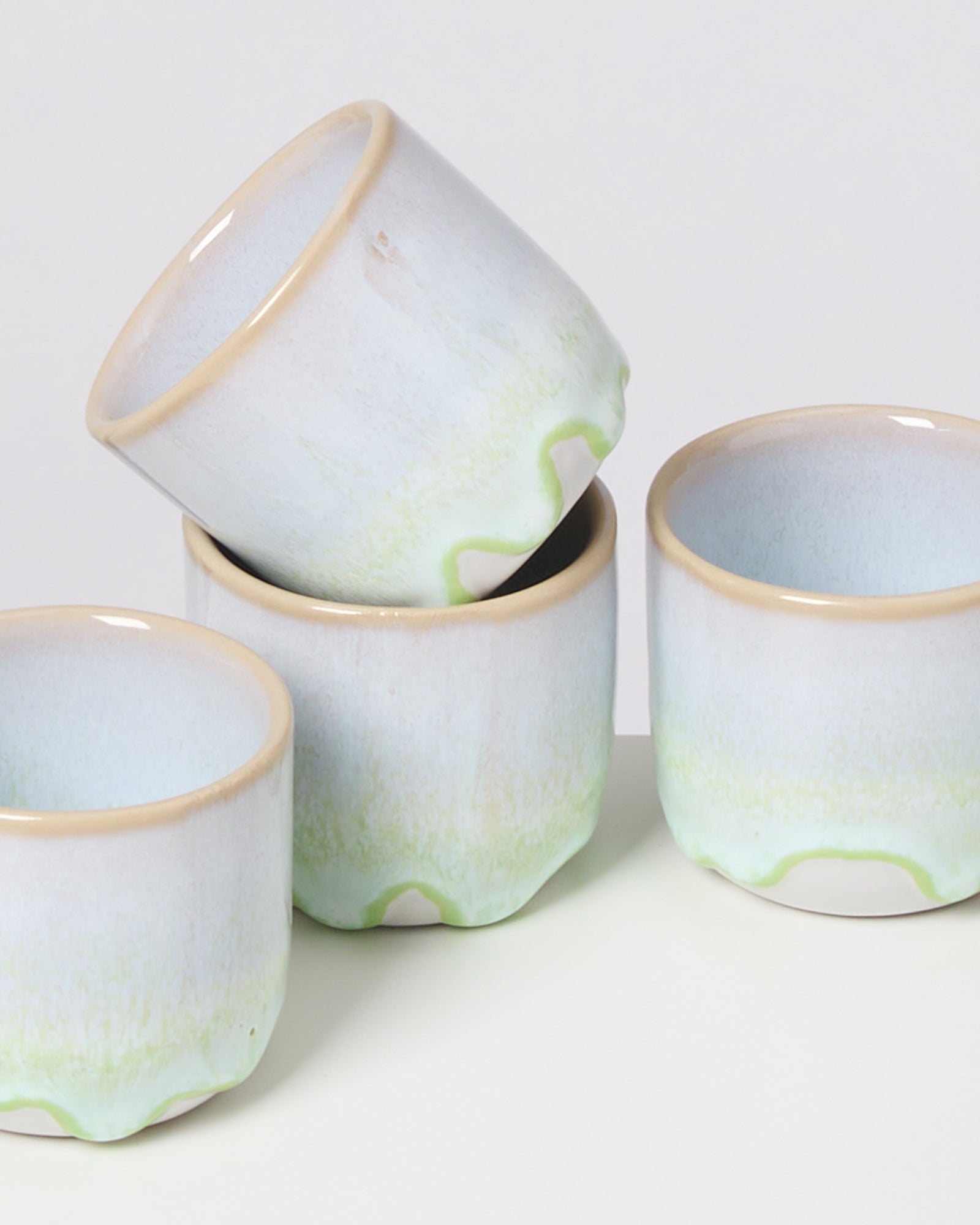 Vier stapelbare, hellblaue Keramiktassen mit grünen Akzenten auf einem weißen Hintergrund.