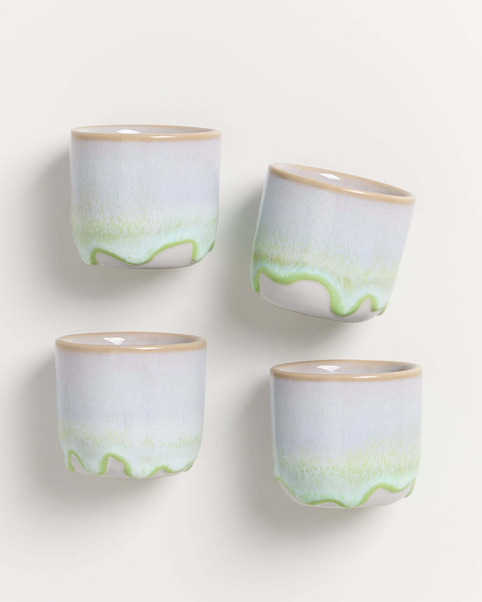 Vier Keramiktassen mit sanften Grün- und Blautönen stehen aufrecht auf einer weißen Oberfläche.