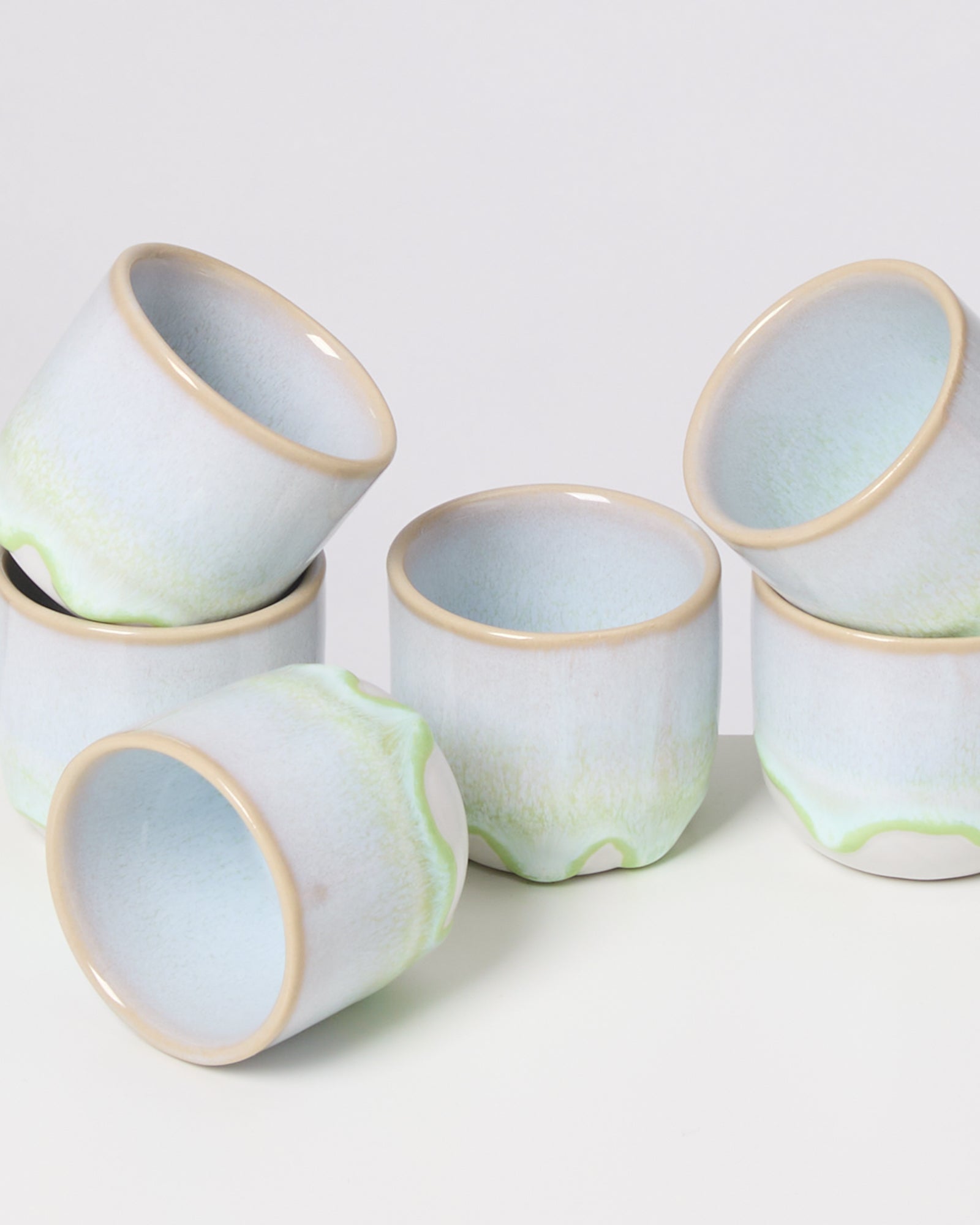 Sechs pastellfarbene Keramiktassen mit leichtem Grün sind ungleichmäßig gestapelt.