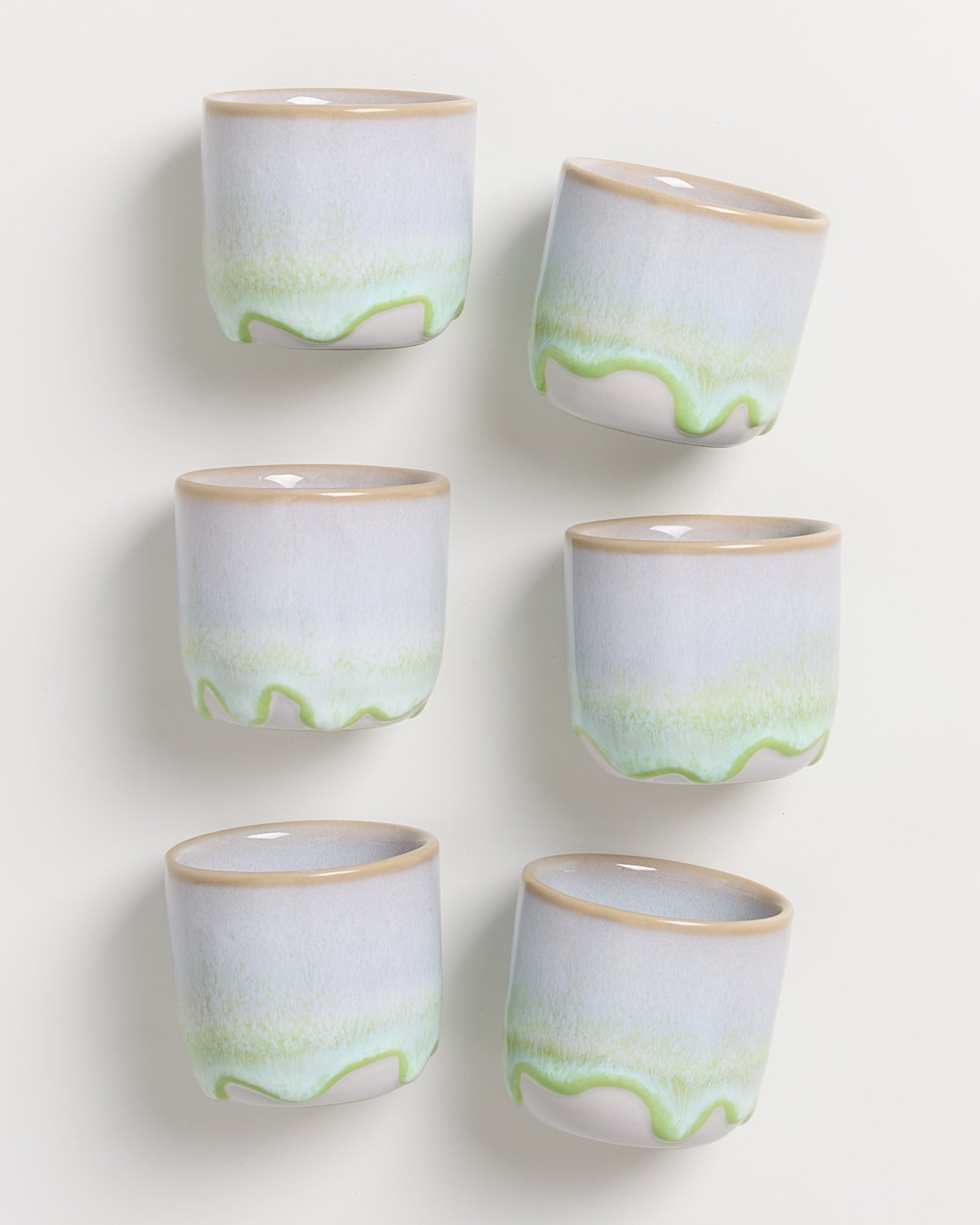 Sechs Keramikbecher mit hellgrauer und grüner Glasur, auf weißem Hintergrund angeordnet.