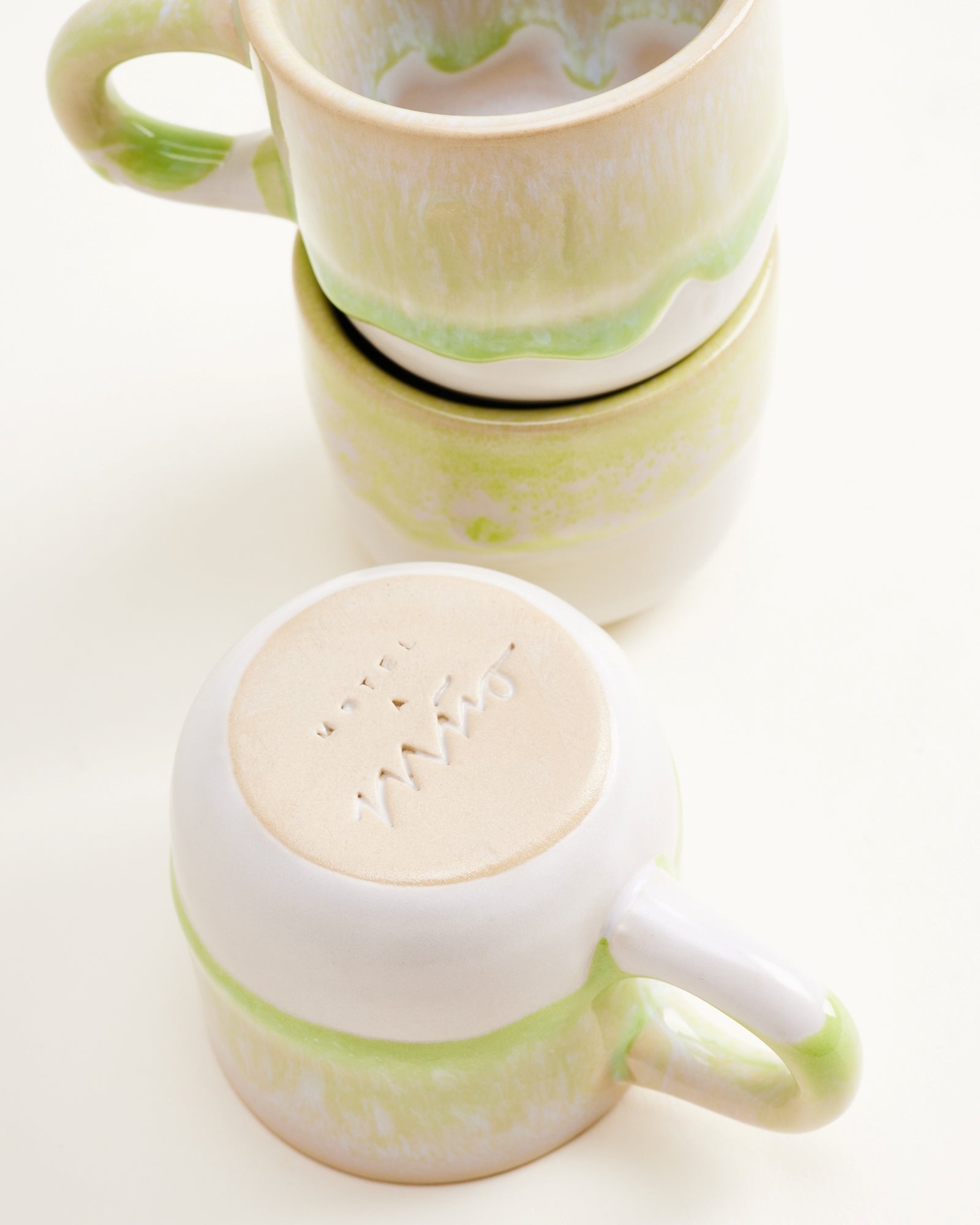 Drei weiße Keramiktassen mit hellgrünen Verzierungen, eine liegt umgedreht mit sichtbarem Bodenstempel.