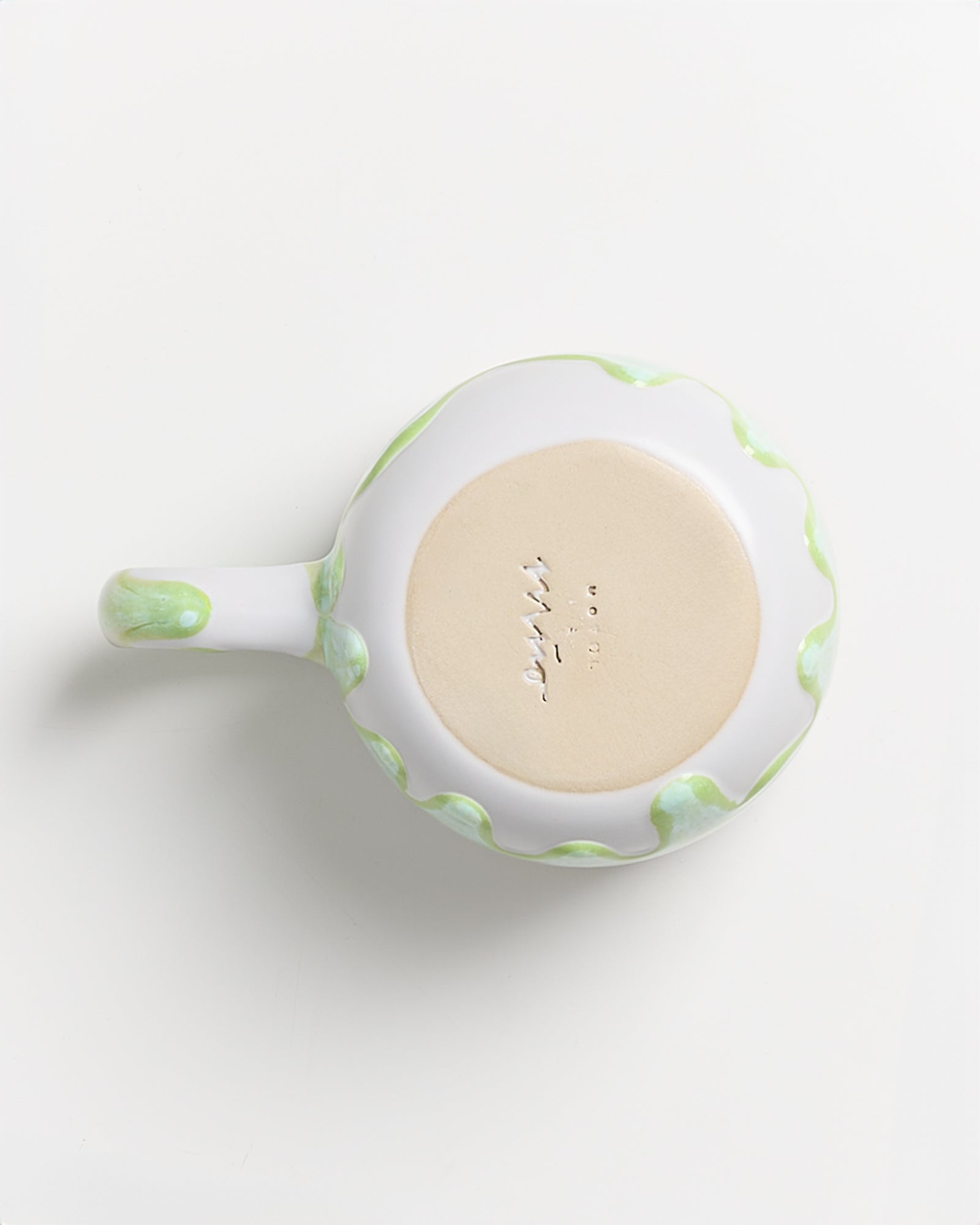 Unteransicht einer weißen Keramiktasse mit grünem Rand und graviertem Boden auf weißem Hintergrund.