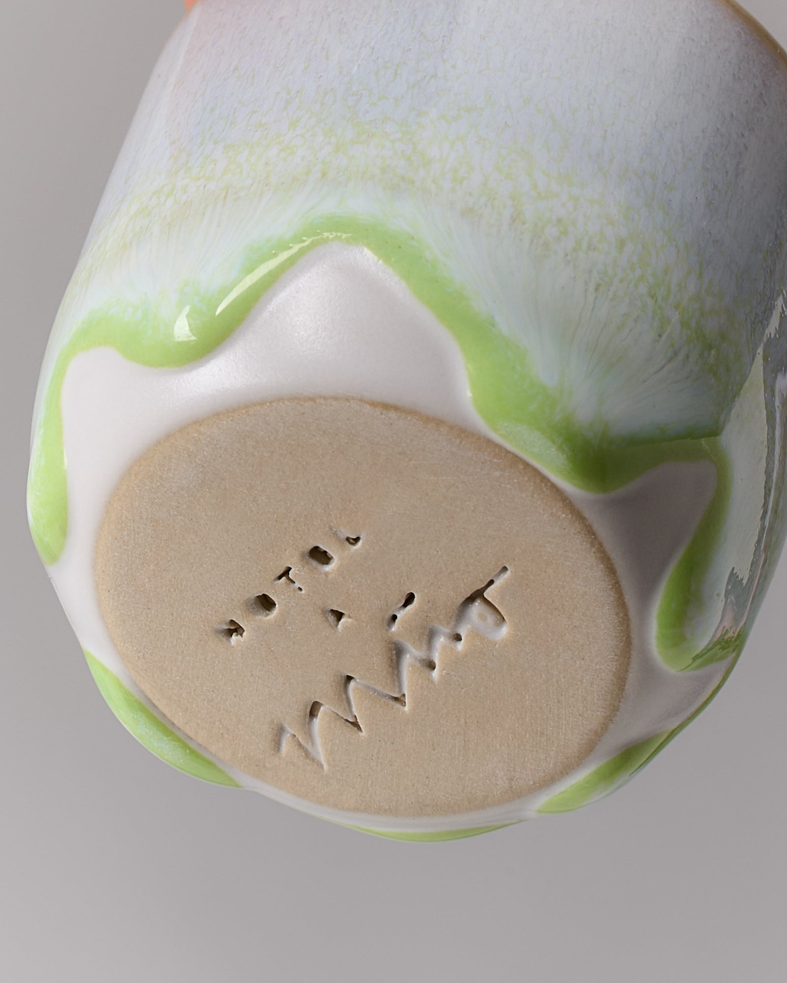 Unterseite eines Keramikbechers mit glasierter grüner Kante und eingestanztem Schriftzug auf hellem Hintergrund.