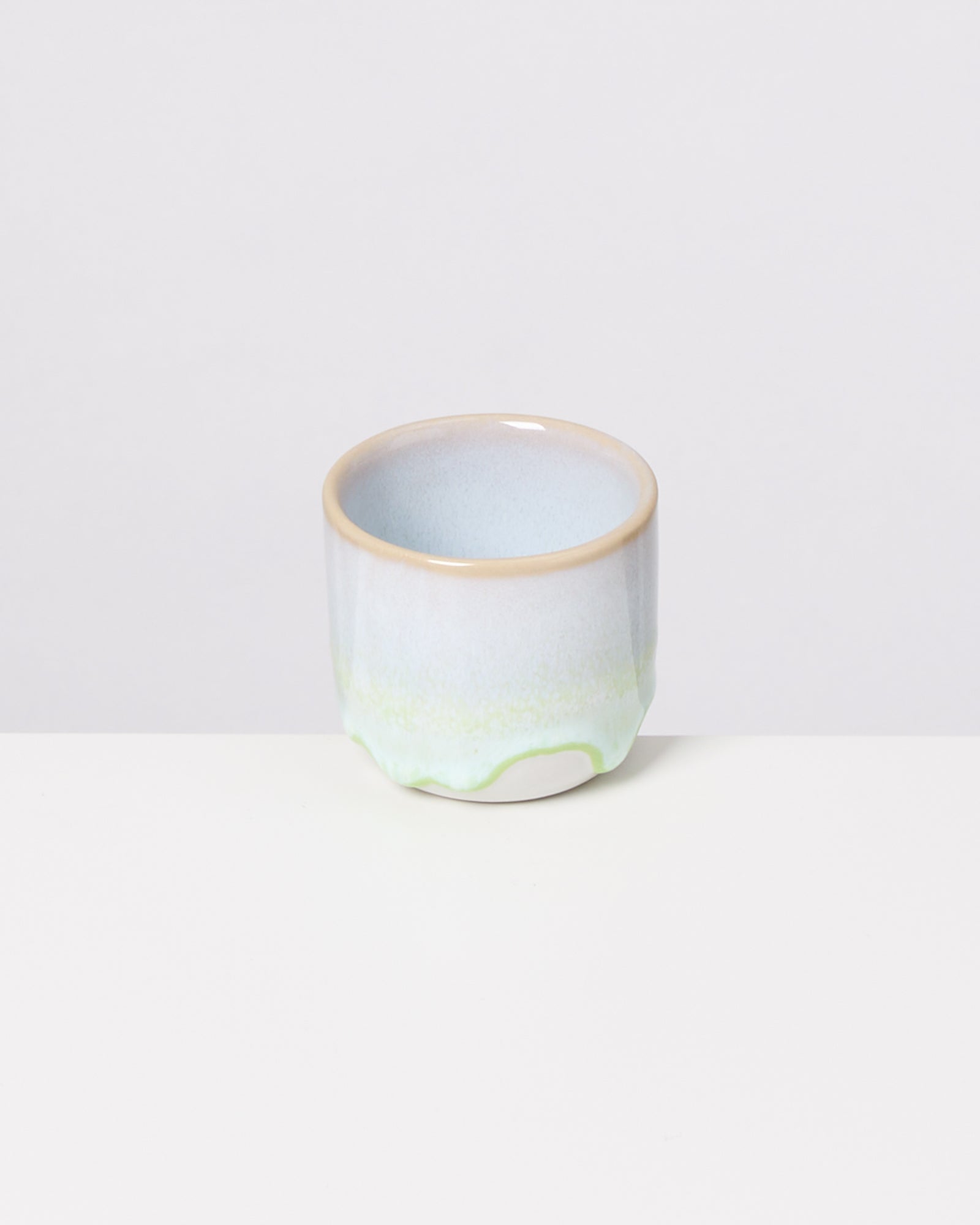 Keramikbecher mit heller blauer und grüner Glasur auf weißem Hintergrund.