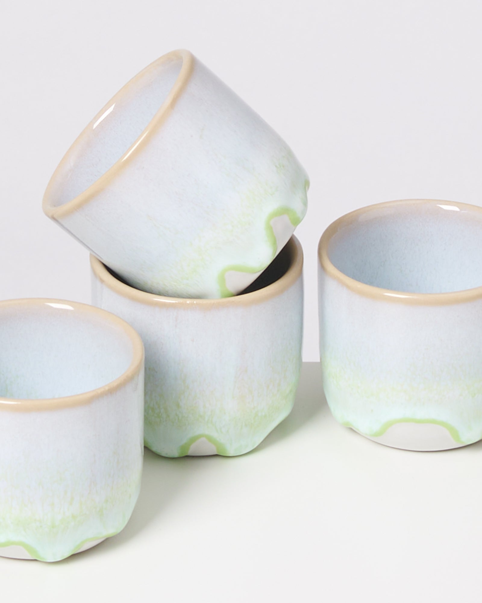 Vier pastellfarbene Keramikbecher mit grünem und beigem Rand stehen und stapeln sich aufeinander.