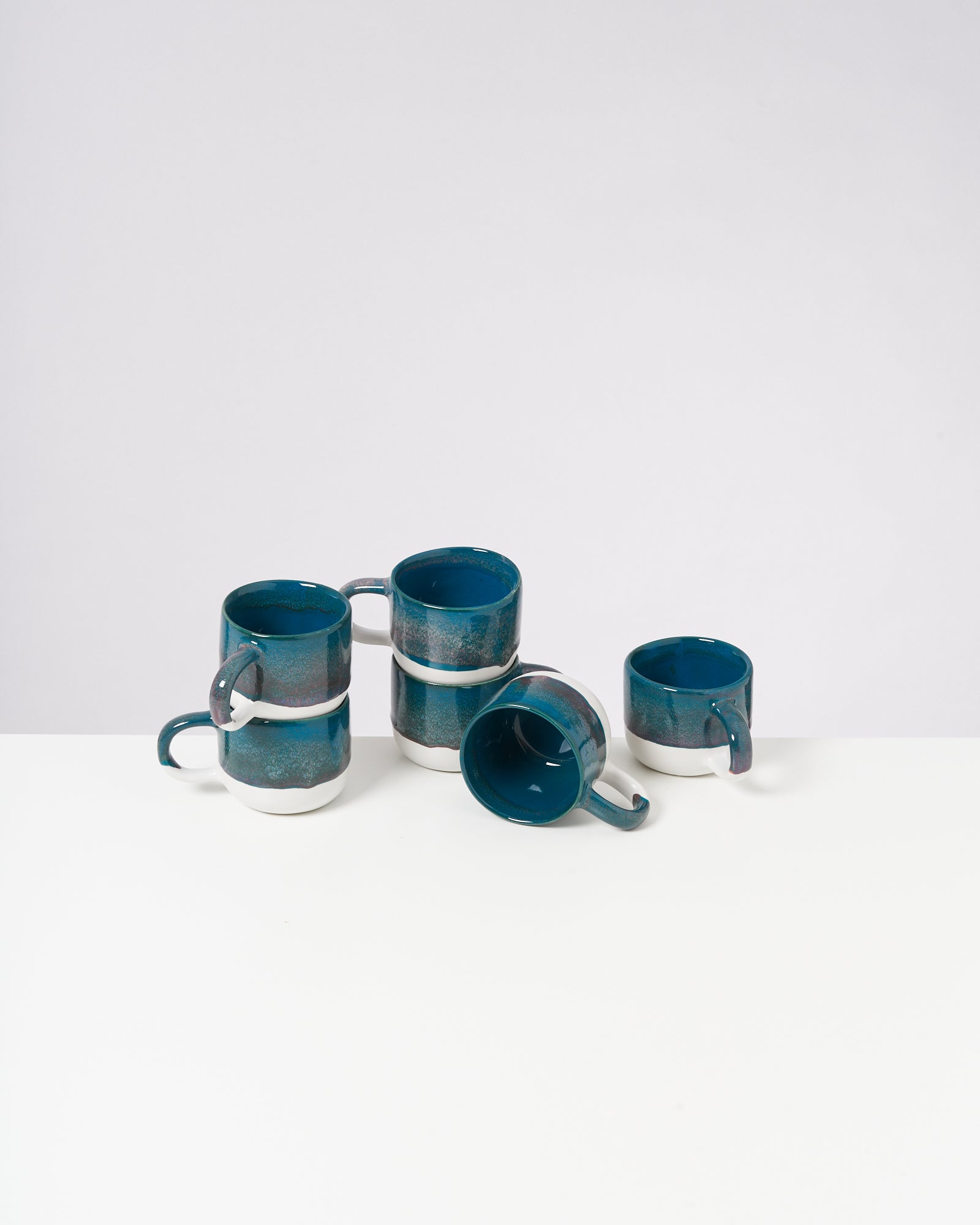 Fünf gestapelte blaue Tassen mit weißem Boden auf einem weißen Tisch vor einem grauen Hintergrund.