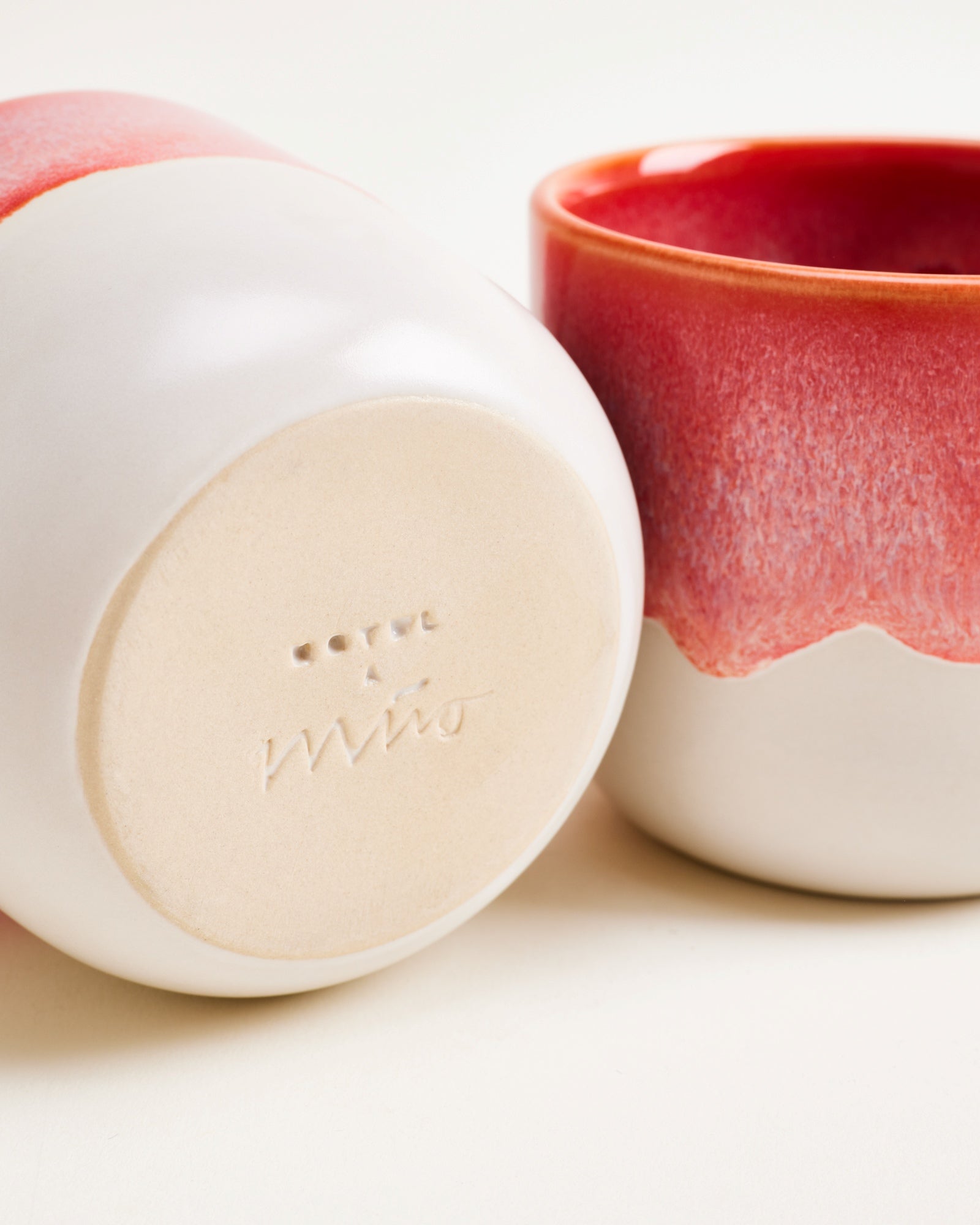 Zwei weiße Keramikgefäße mit roten Akzenten, eines liegt auf der Seite, das andere steht aufrecht.