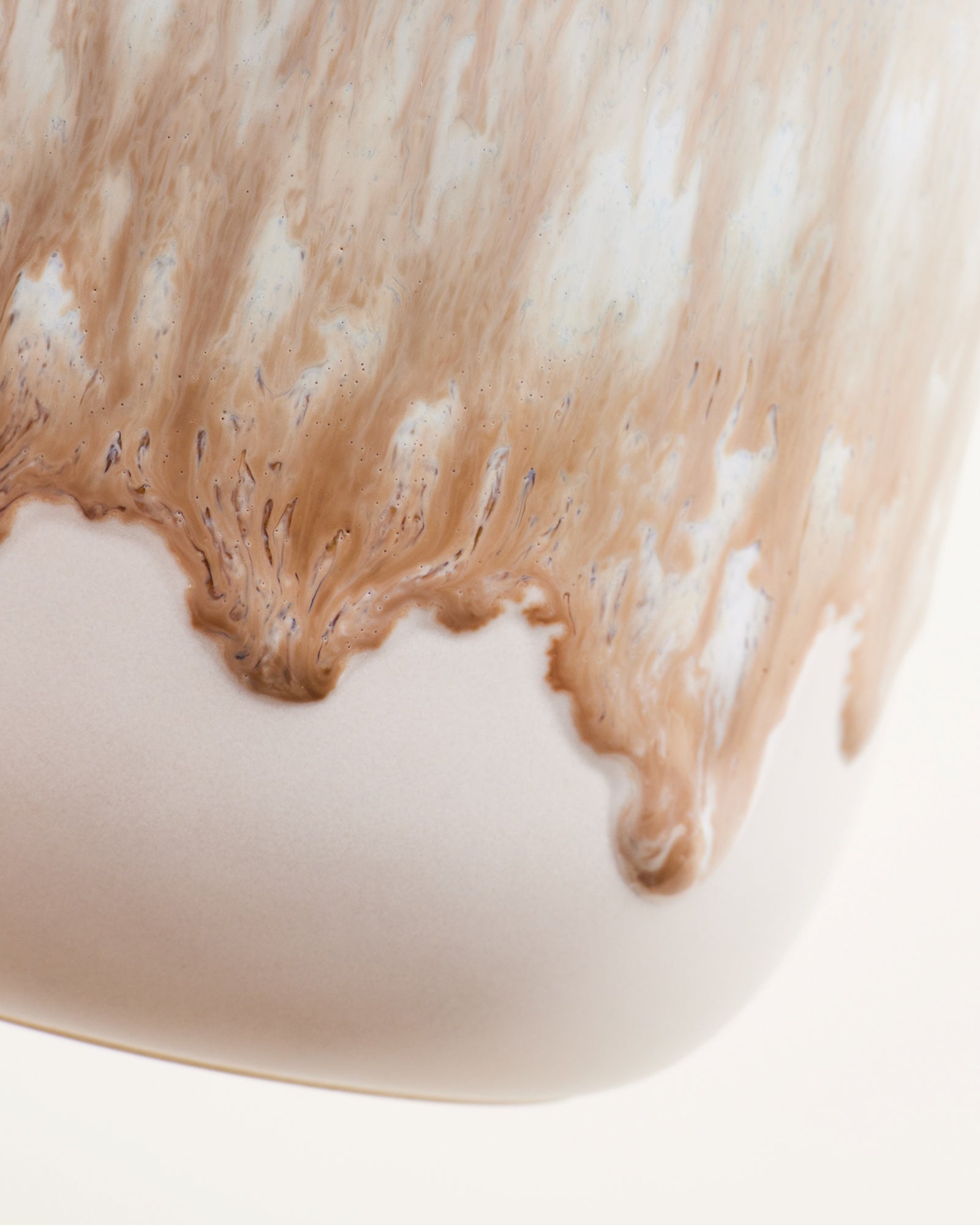 Nahaufnahme einer Keramikoberfläche mit fließendem, beige-braunen Glasureffekt.