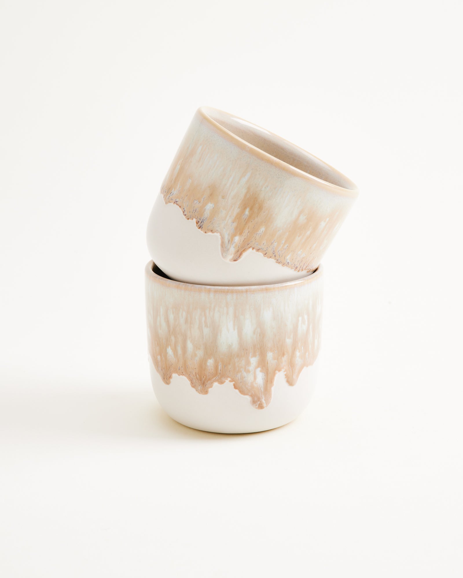 Zwei übereinander gestapelte Keramikbecher mit brauner, tropfenförmiger Glasur auf weißem Hintergrund.