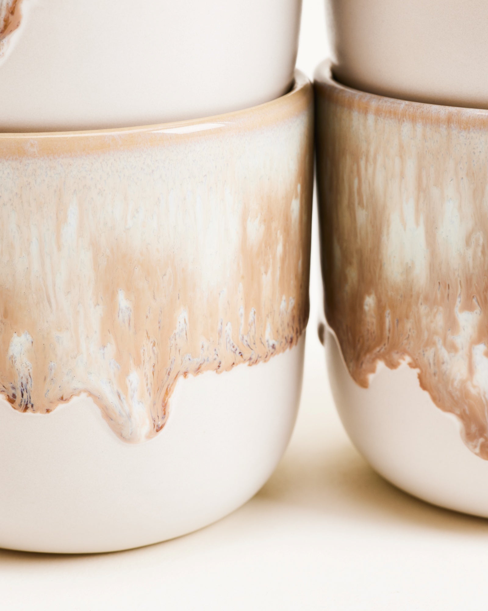 Nahaufnahme von zwei gestapelten Bechern mit beige-weißem, tropfendem Glasurmuster.