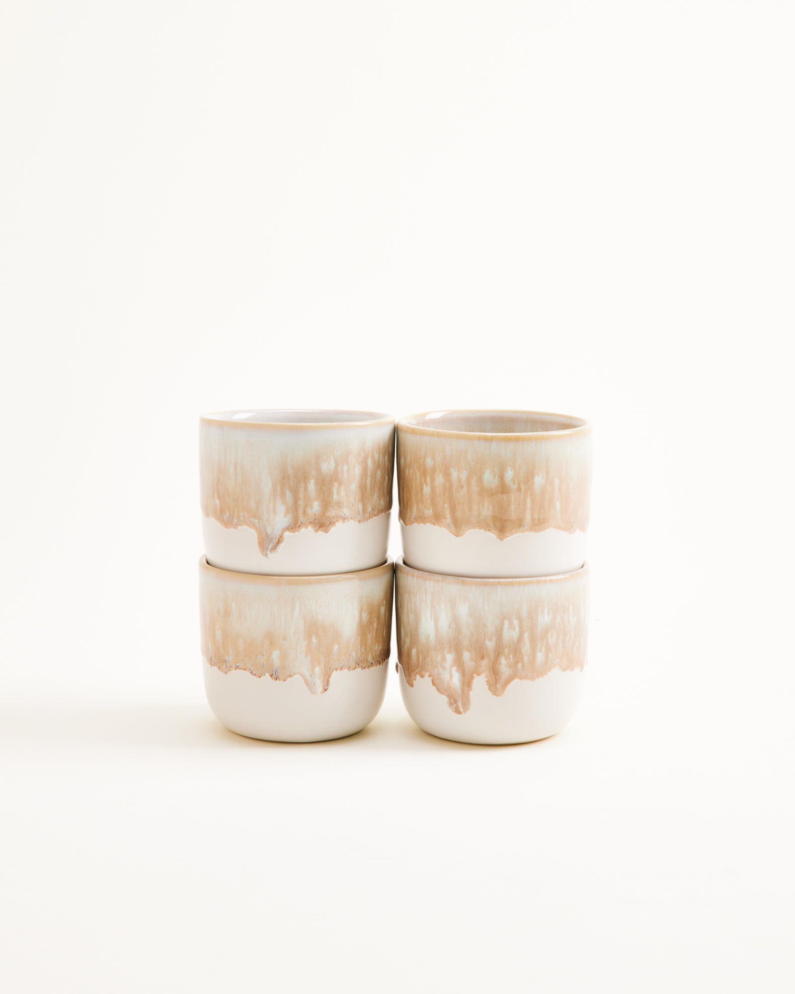 Vier gestapelte, cremefarbene Keramikbecher mit braunen, tropfartigen Akzenten vor weißem Hintergrund.